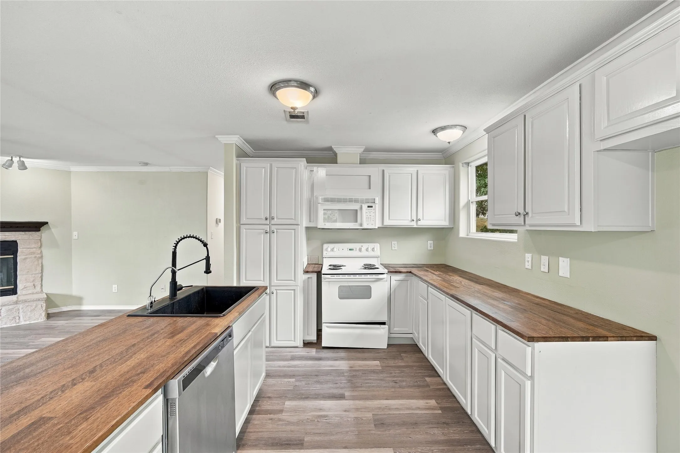 Kitchen featuring white cabinetry, wood-finish countertops, a black farm sink with a gooseneck faucet, and stainless steel dishwasher