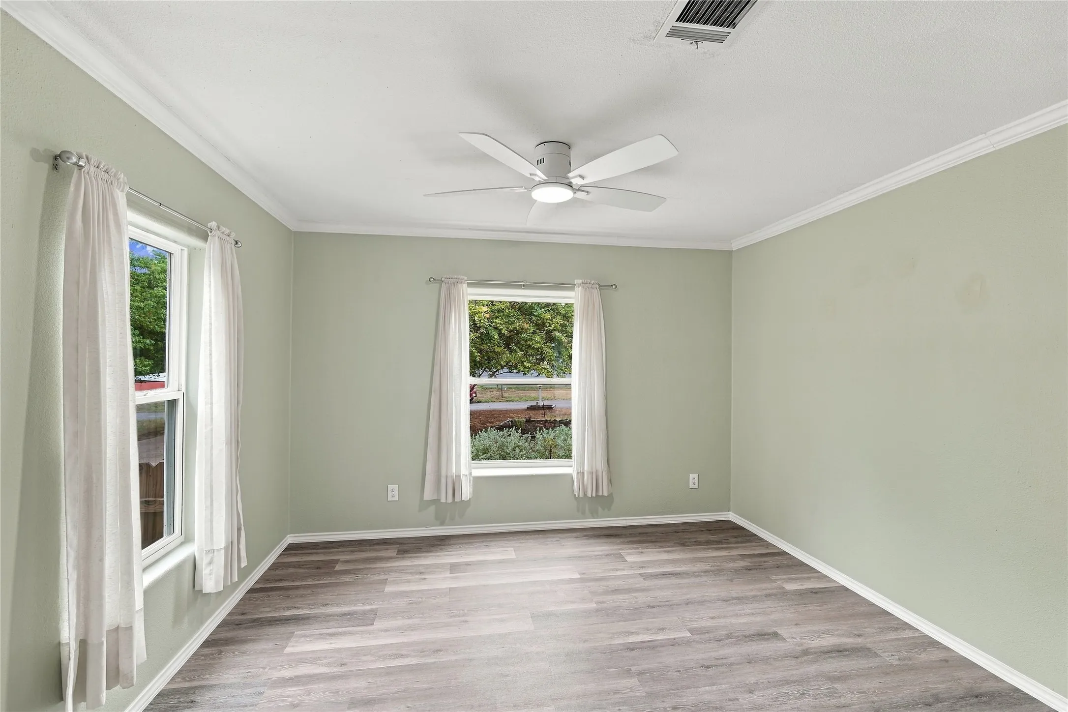 Wood-look flooring, crown molding, two windows, and a ceiling fan with integrated lighting