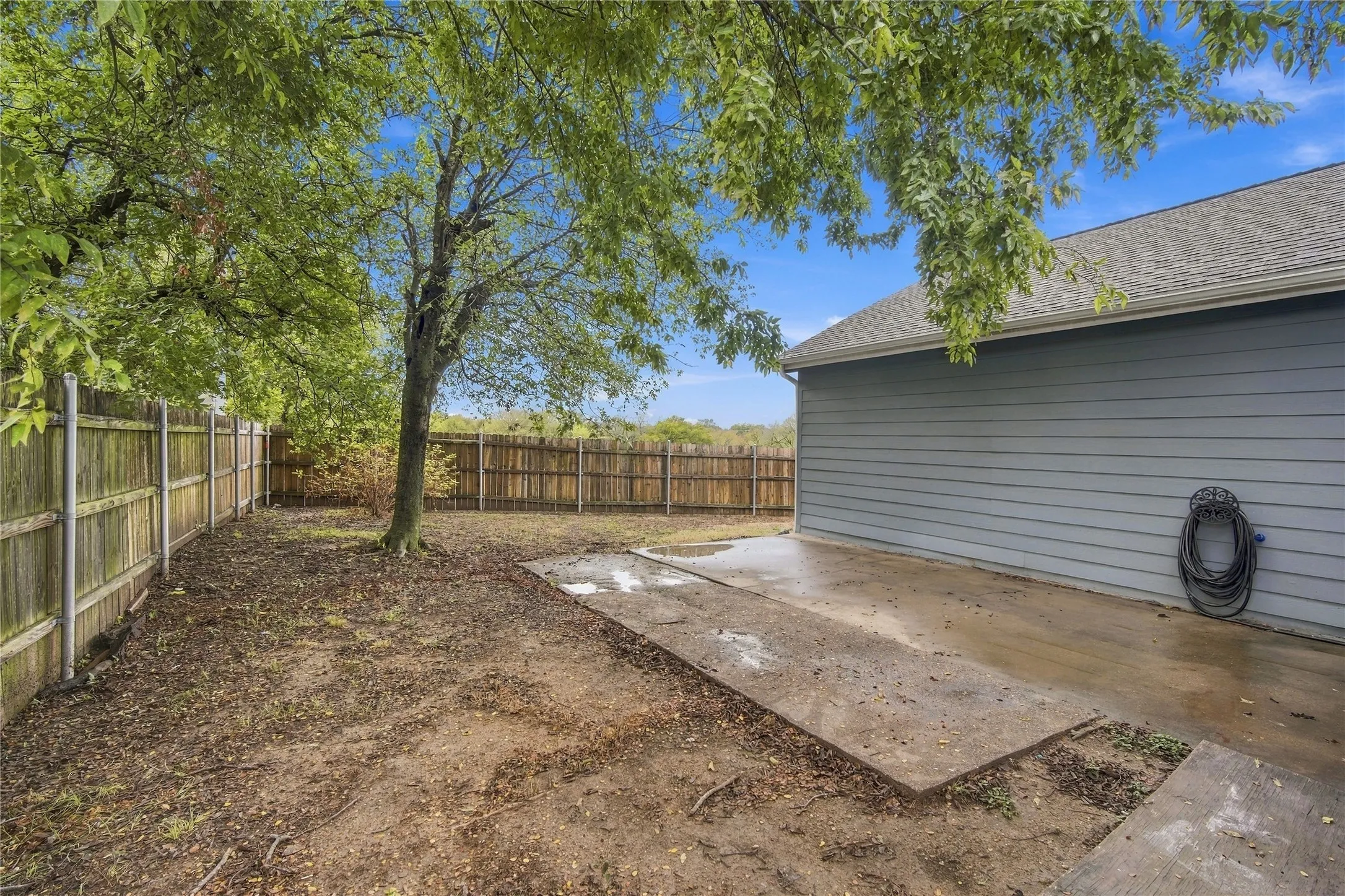Private fenced backyard with mature trees, a concrete patio, and a 2025 roof