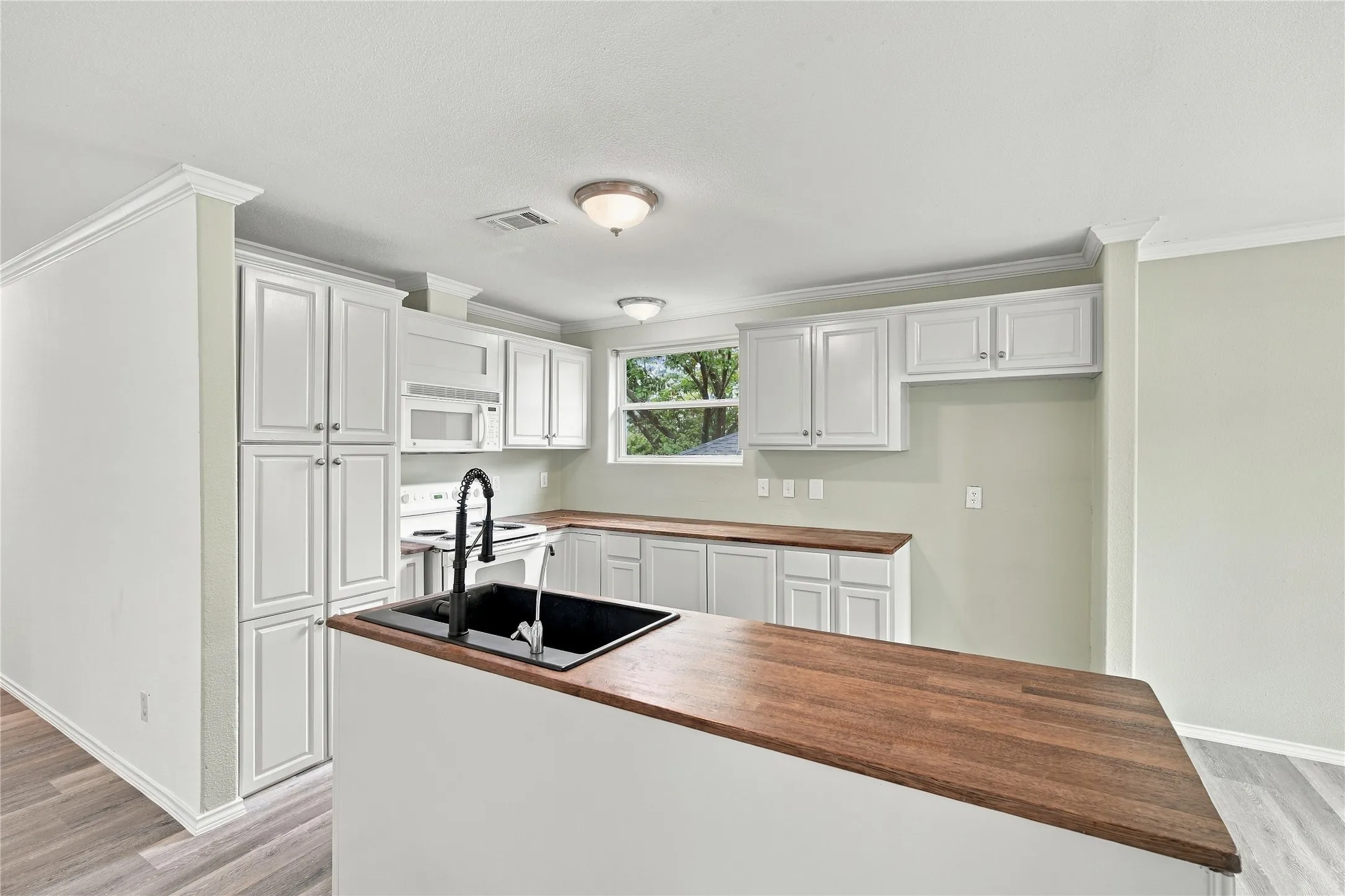 Kitchen featuring white cabinetry, wood-finish countertops, black farm sink with gooseneck faucet, microwave, and range