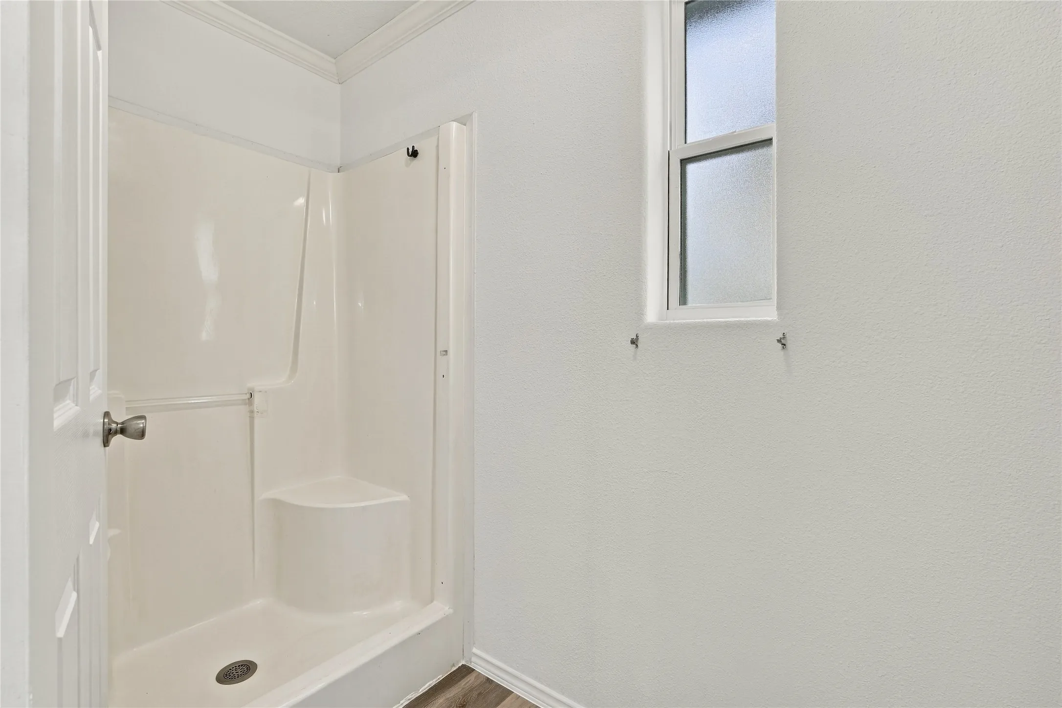 White shower stall with a built-in seat, a frosted glass window, and wood-look flooring