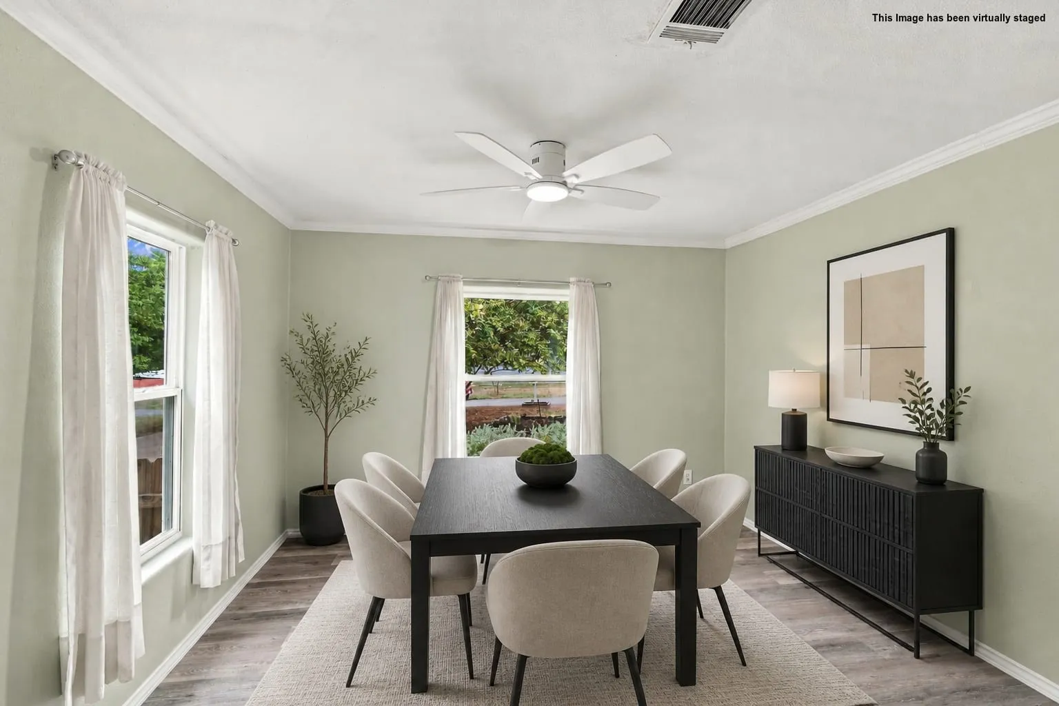Virtually staged. Crown molding accents, wood-finish flooring, two large windows, ceiling fan with integrated lighting, and a built-in sideboard