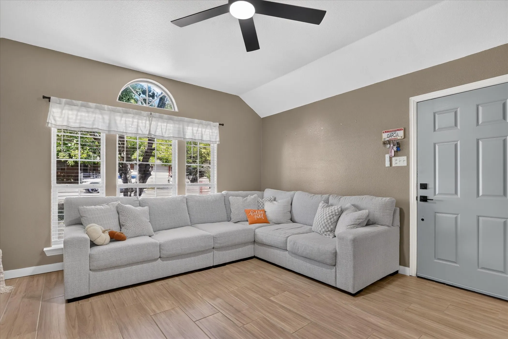 Vaulted ceiling with a black ceiling fan, wood-finish flooring, and a window with an arched transom