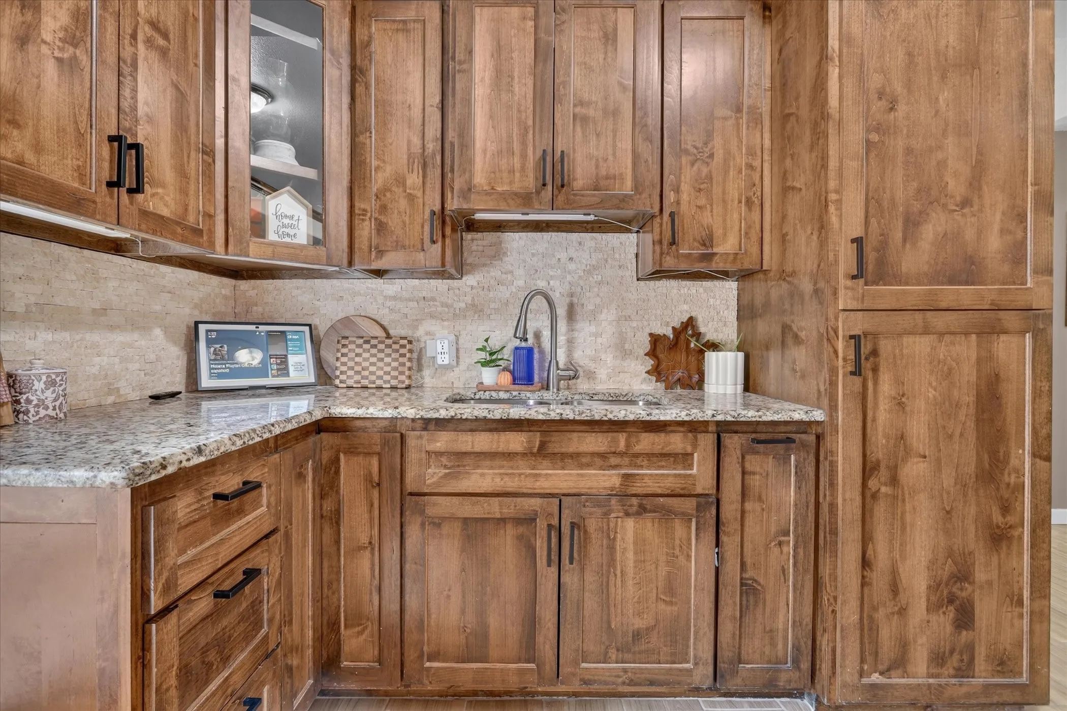 Wood-finish cabinetry with black hardware, light-toned stone countertops, and a tile backsplash
