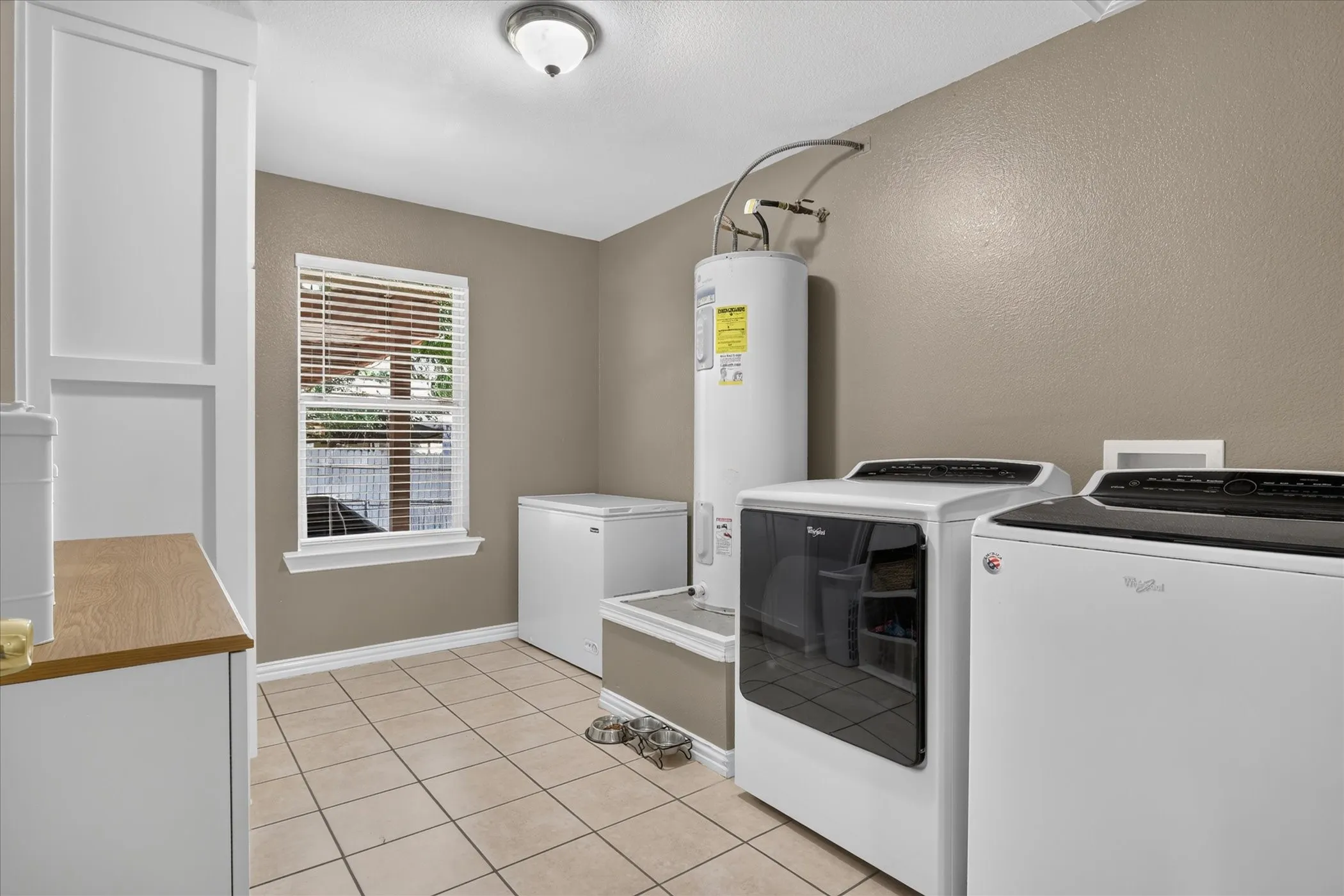 Tile flooring, built-in cabinetry with wood-finish countertop, window with blinds, overhead lighting, and neutral wall paint