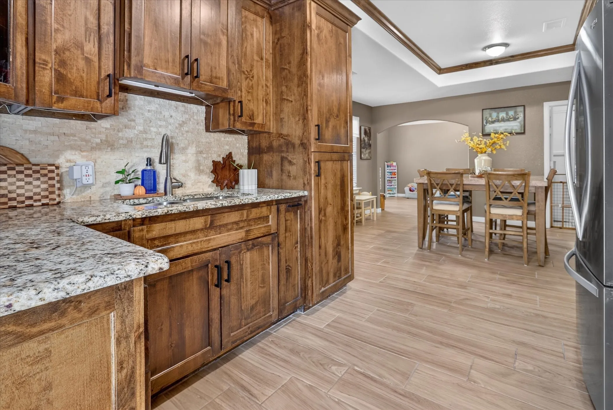 Kitchen featuring wood cabinetry, granite countertops, a stainless steel sink with a gooseneck faucet, and a stone-finish backsplash