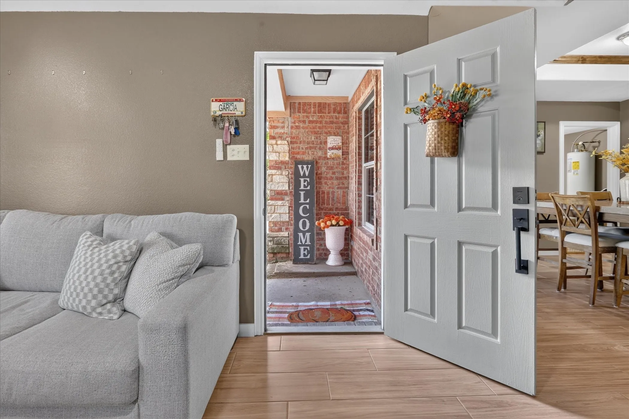 Six-panel entry door with matte black hardware, wood-finish flooring, and brick exterior detailing