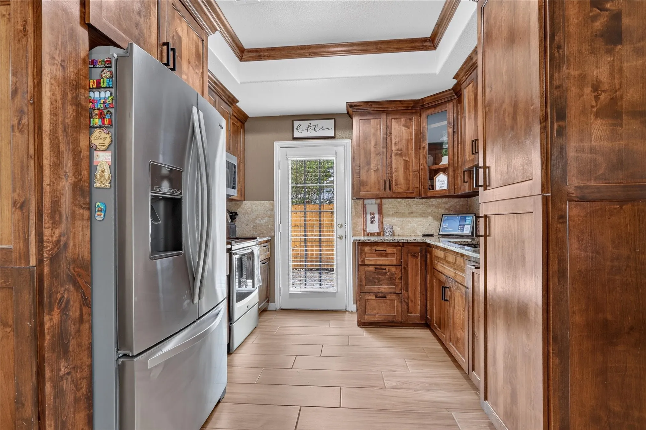 Wood-finish flooring, stainless steel appliances, wood cabinetry, stone countertop, and a glass-paneled door