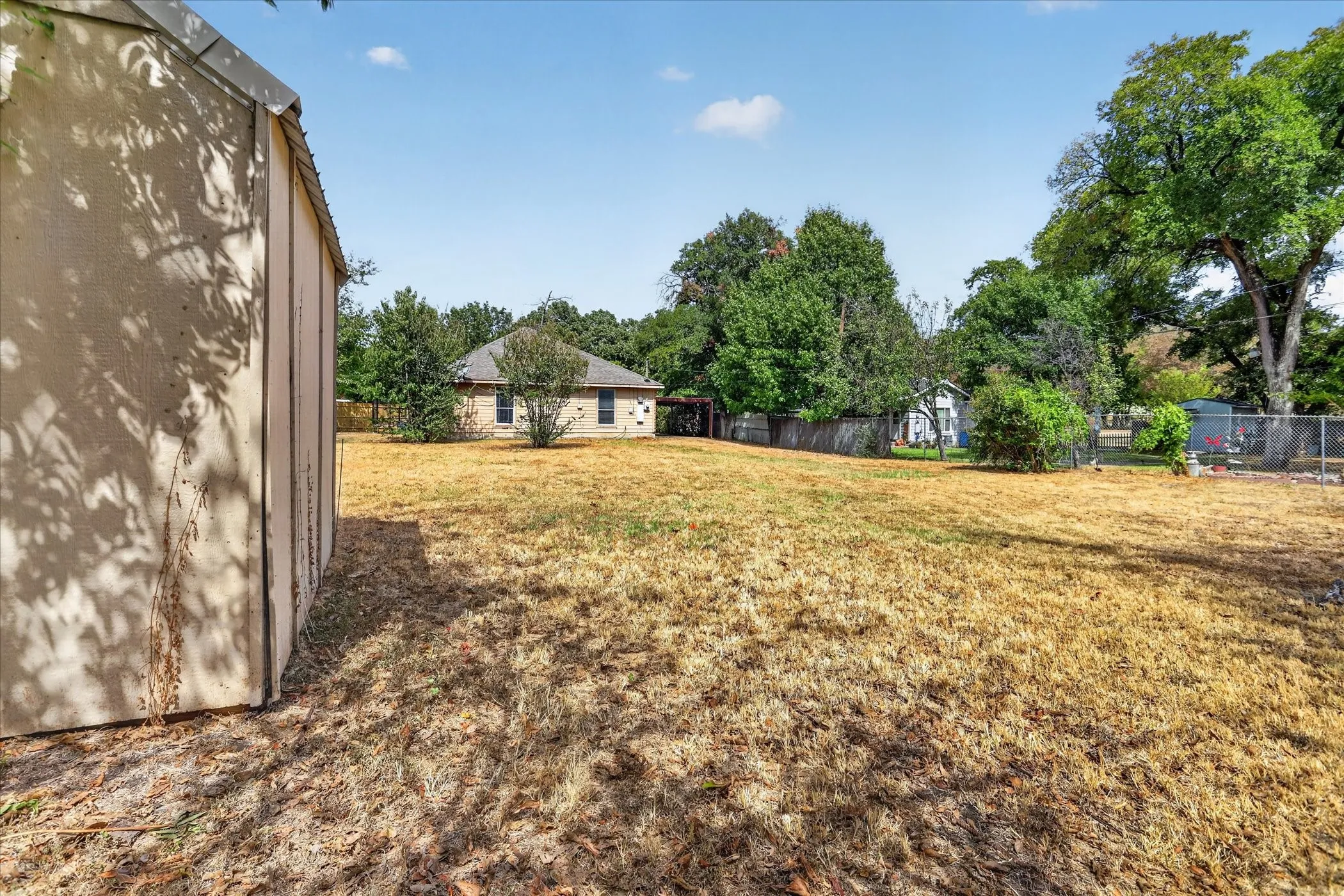 Expansive backyard featuring a storage shed, established trees, and a chain-link fence