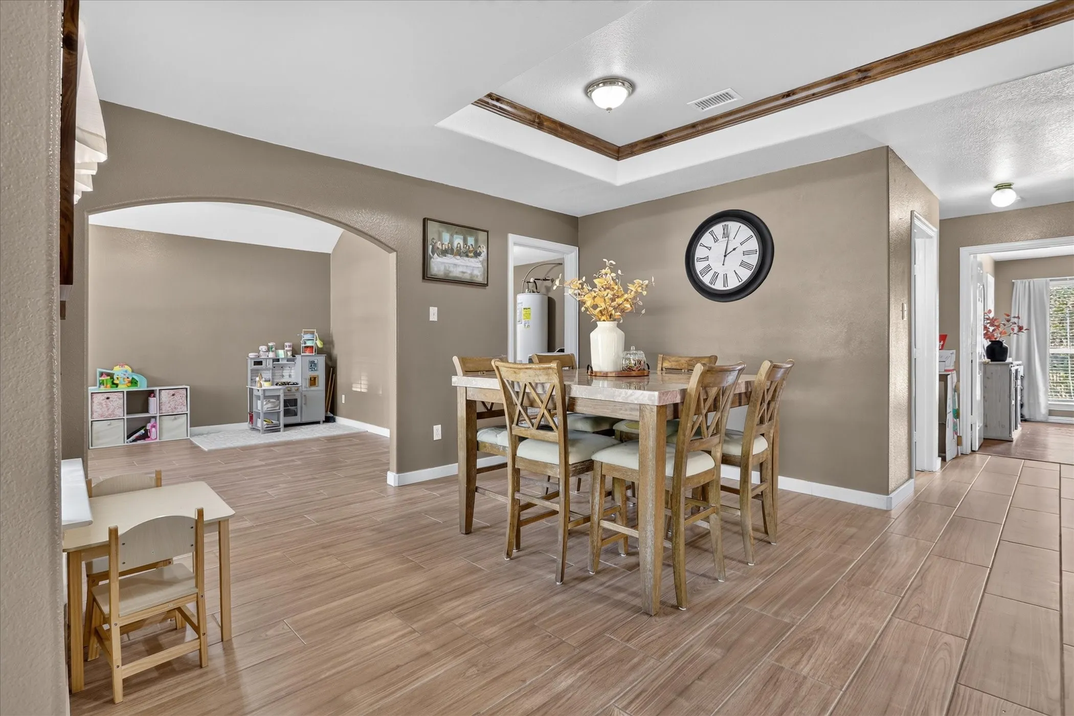 Wood-finish flooring throughout, tray ceiling with wood-clad trim, recessed lighting, and arched doorway