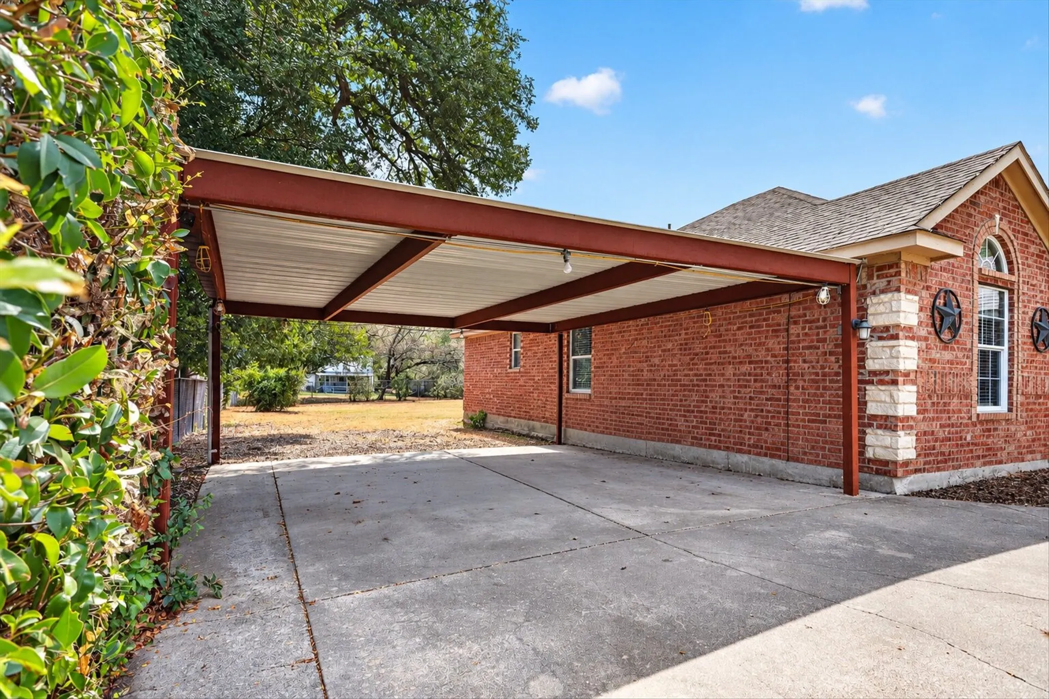 Attached carport structure, concrete driveway, brick exterior with stone accents, arched window, and exterior wall sconces