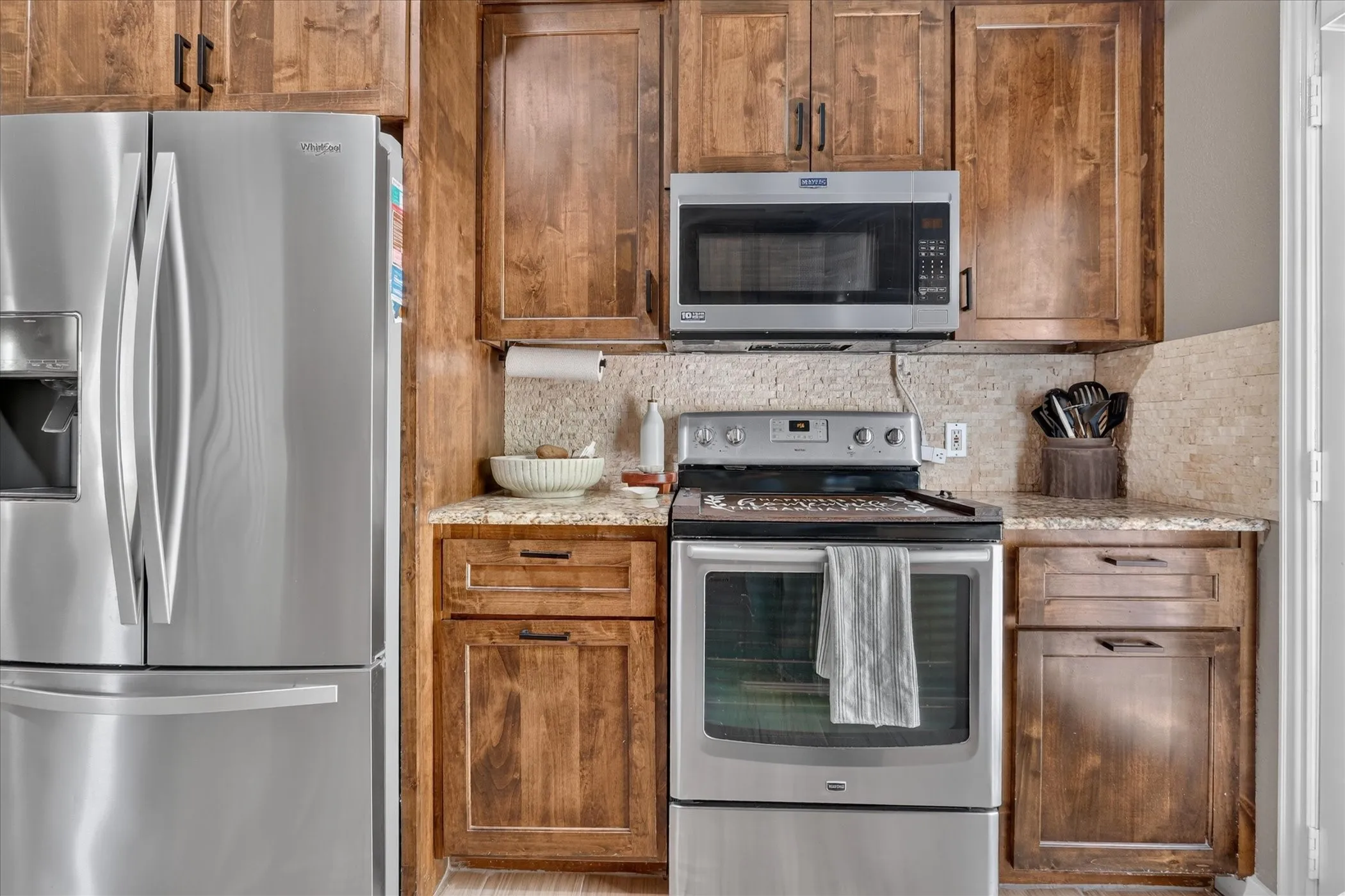 Stainless steel refrigerator, coordinating stainless steel range, built-in stainless steel microwave, wood-finish cabinetry, and stone-look countertops