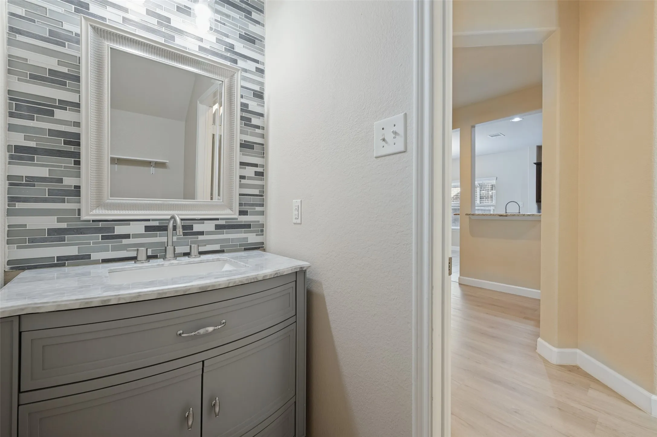 Vanity with gray cabinet and integrated sink, marble-finish countertop, and decorative tile backsplash