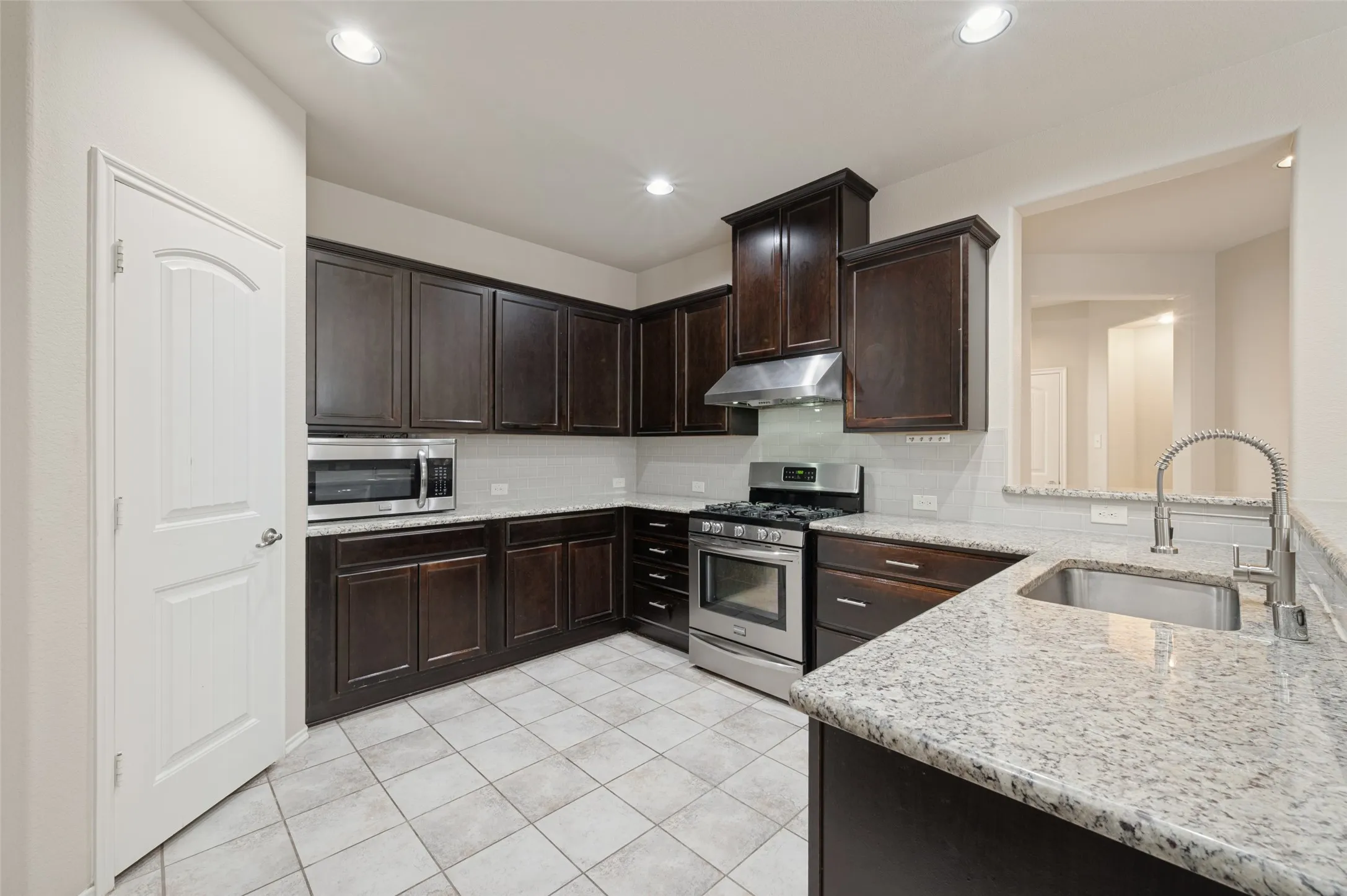 Kitchen featuring dark wood cabinetry, light-colored granite countertops, and stainless steel appliances including a range and microwave