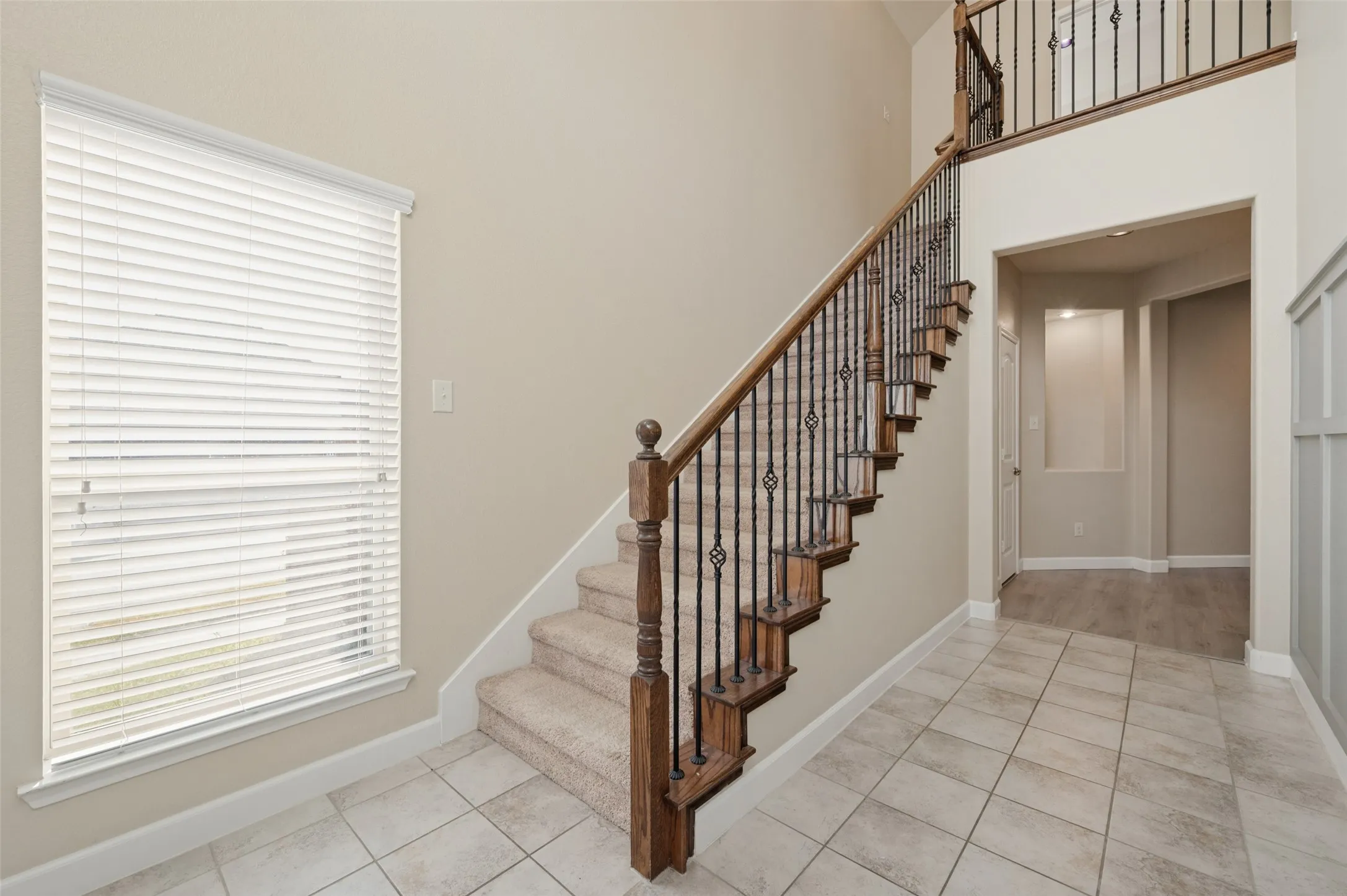 Two-story entryway with a carpeted staircase featuring an ornate wrought iron and wood banister