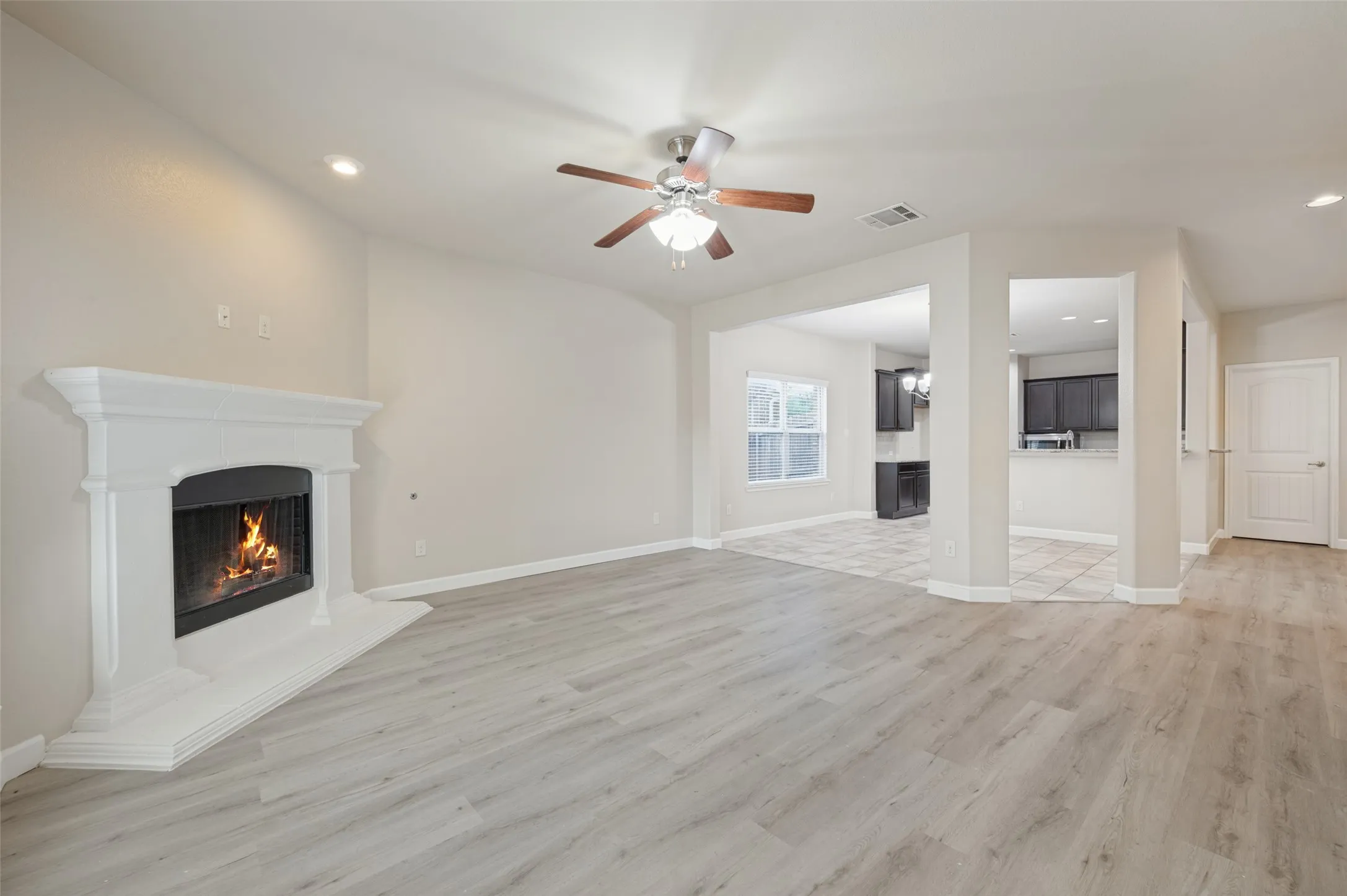 Spacious room featuring wood-finish flooring, a white mantel fireplace, recessed lighting, and a ceiling fan