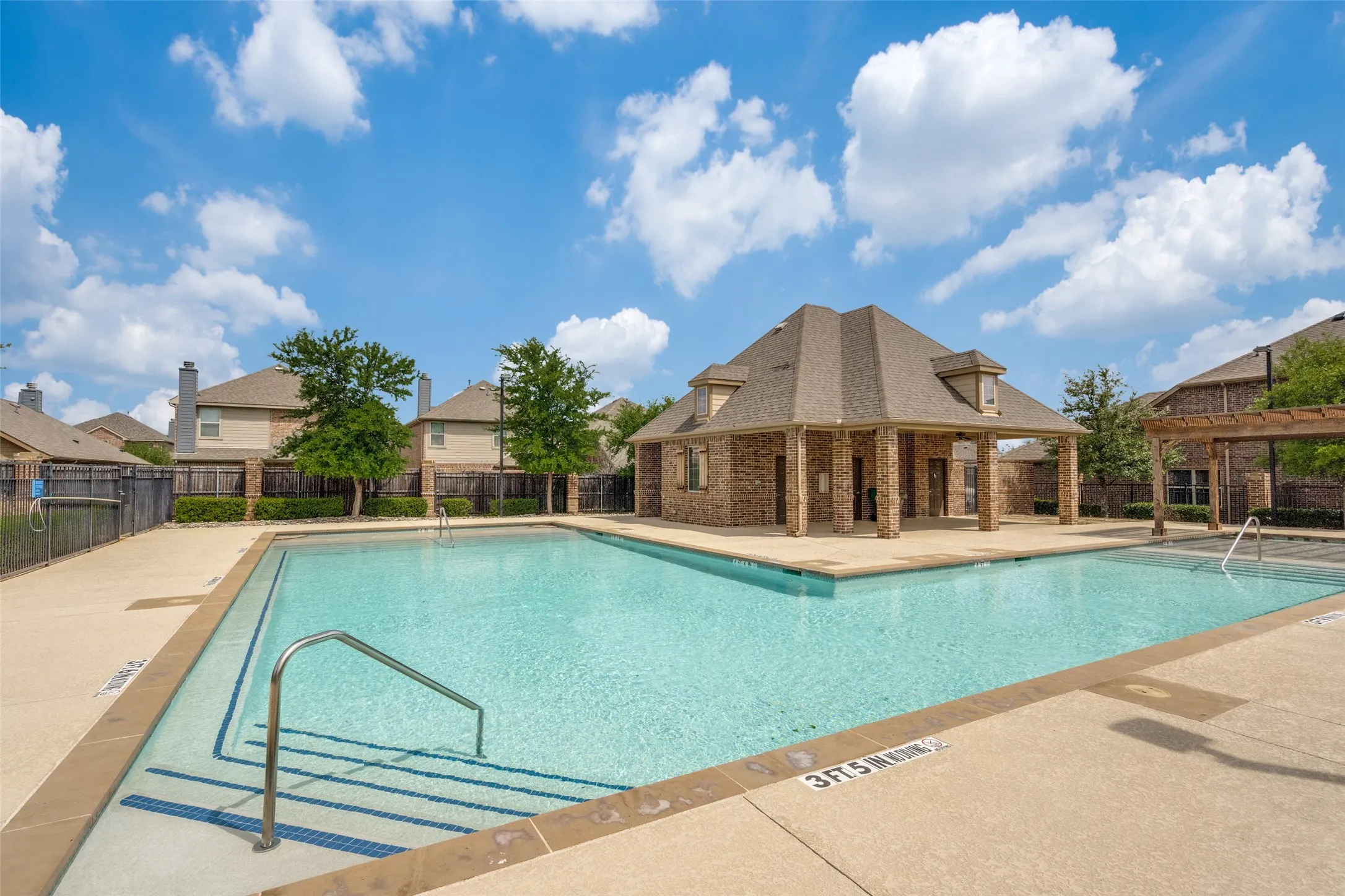 Community swimming pool with concrete decking, a brick and shingle pavilion, and metal handrails