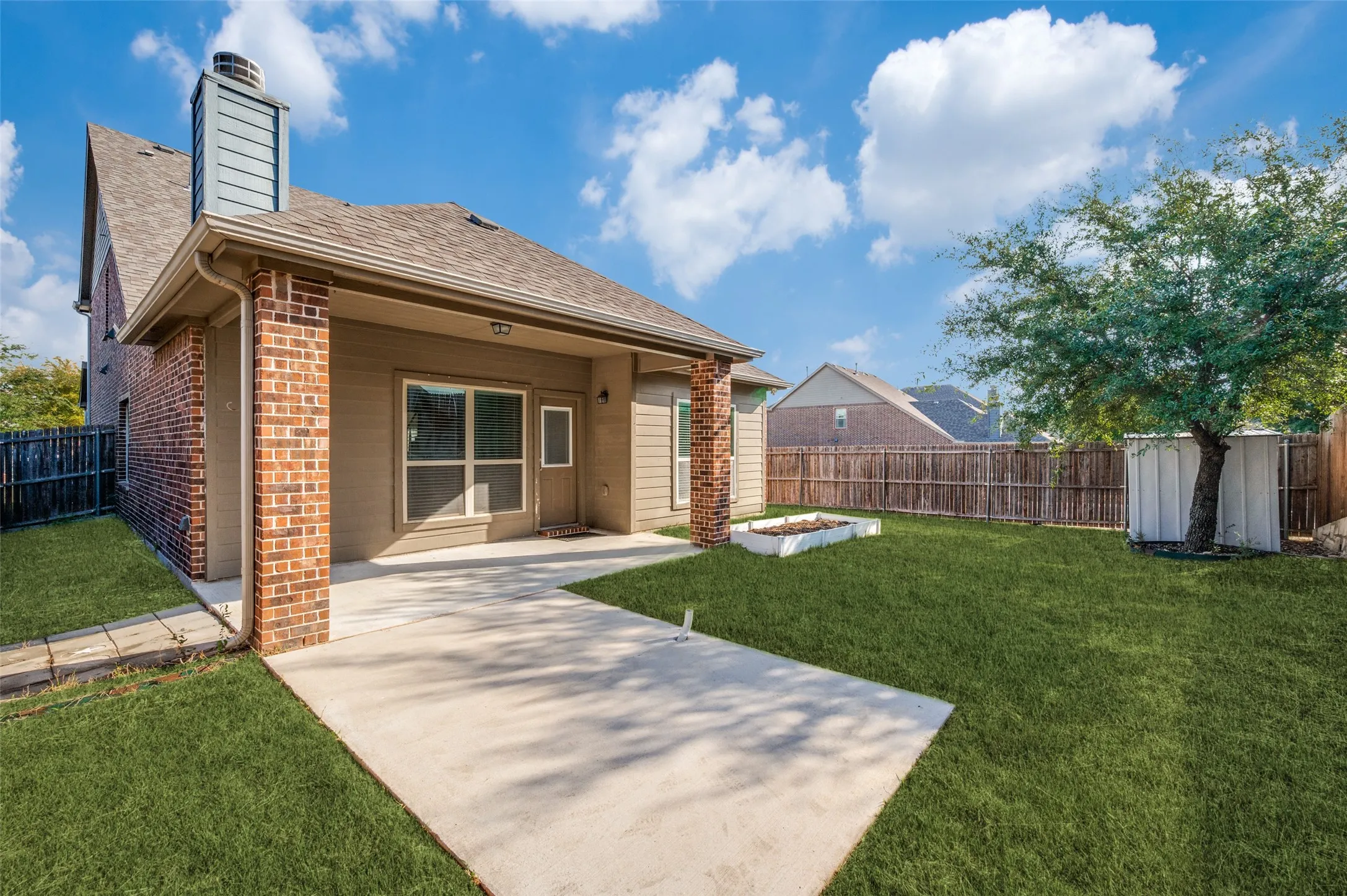 Expansive backyard featuring a concrete patio, brick columns, mature tree, and privacy fencing