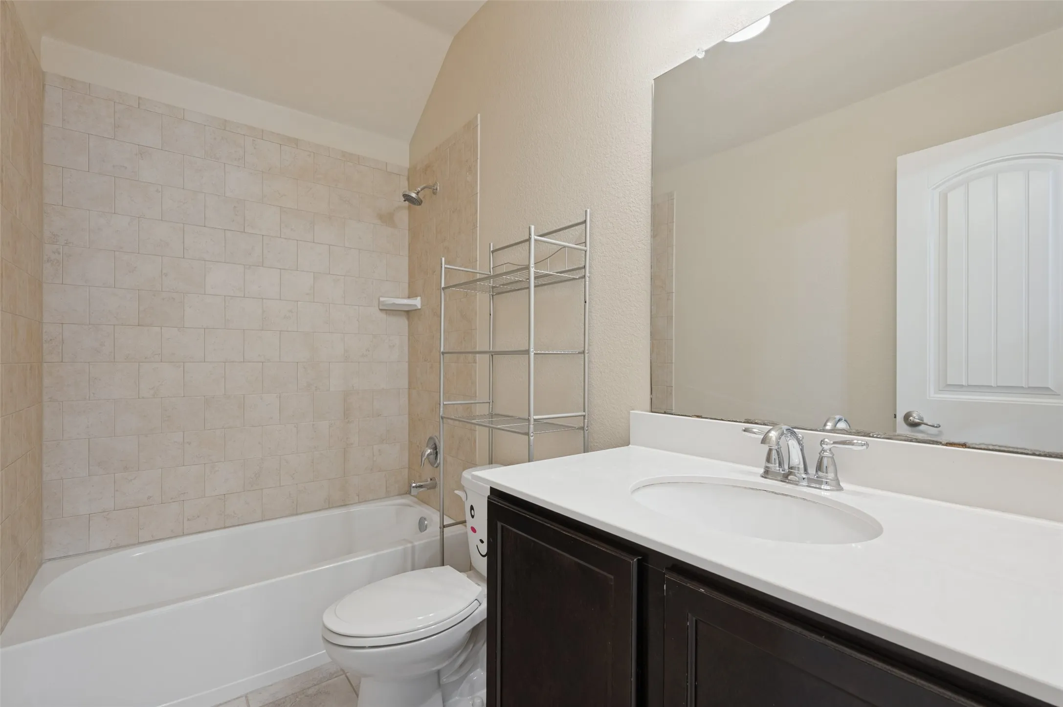 Bathroom featuring a white bathtub, tiled shower surround, dark wood-finish vanity with an integrated sink, and a large wall-mounted mirror