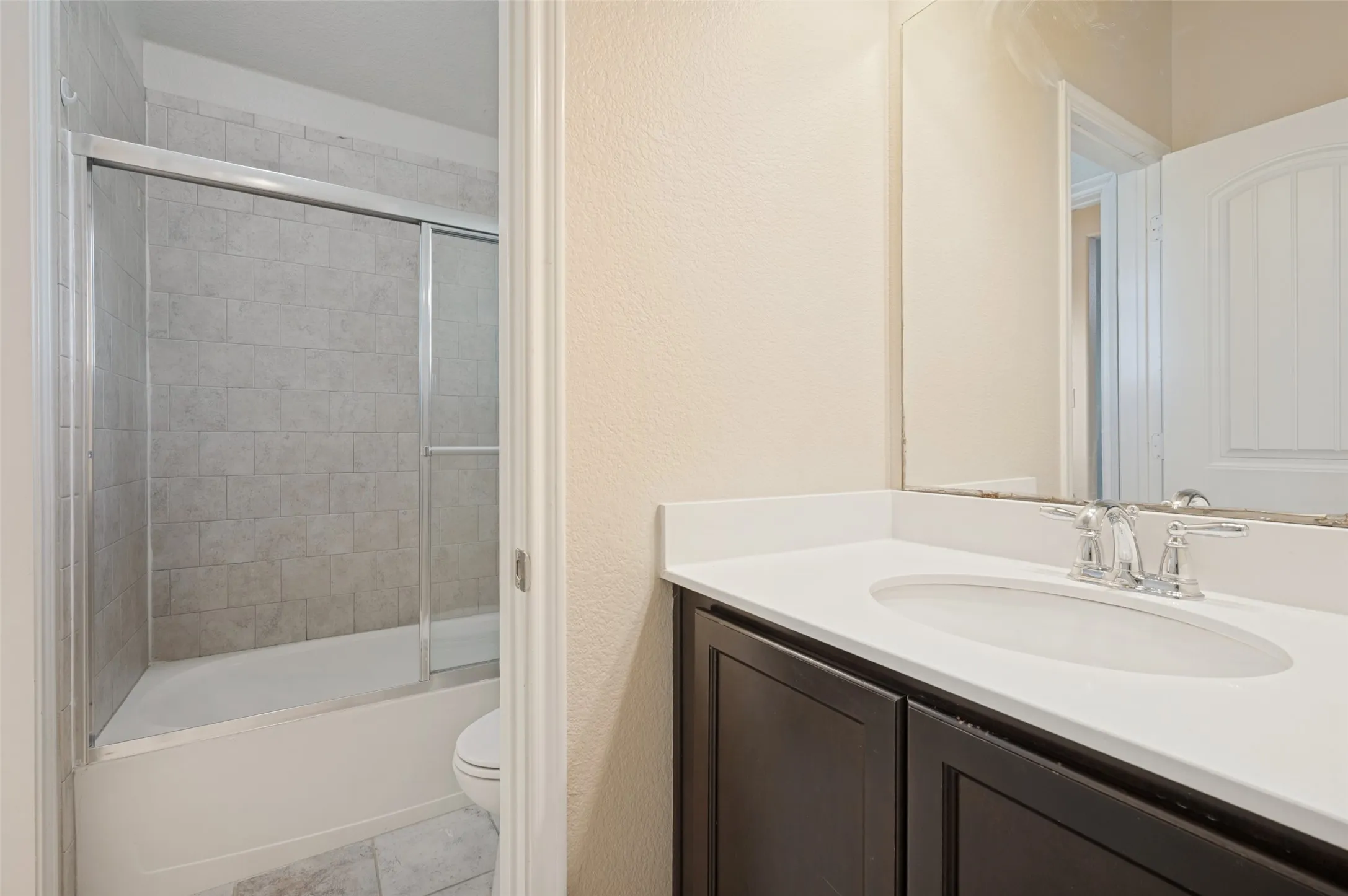 Bathroom featuring a dark wood-finish vanity with an integrated white sink, chrome faucet, and a large mirror