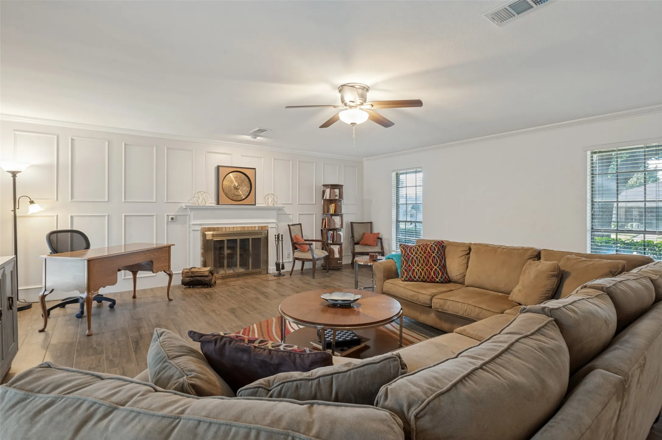 Wood-finish flooring throughout, a white paneled accent wall, a built-in fireplace with an ornate mantel, and a ceiling fan with integrated lighting