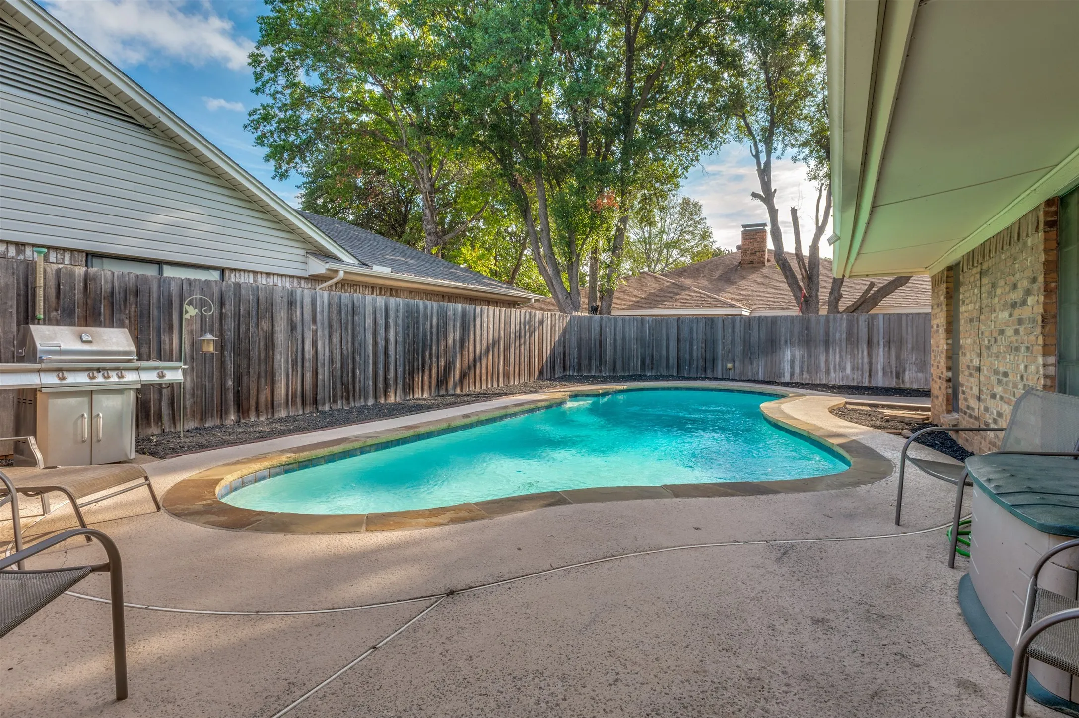 Outdoor swimming pool with a concrete deck, wood privacy fence, and covered patio