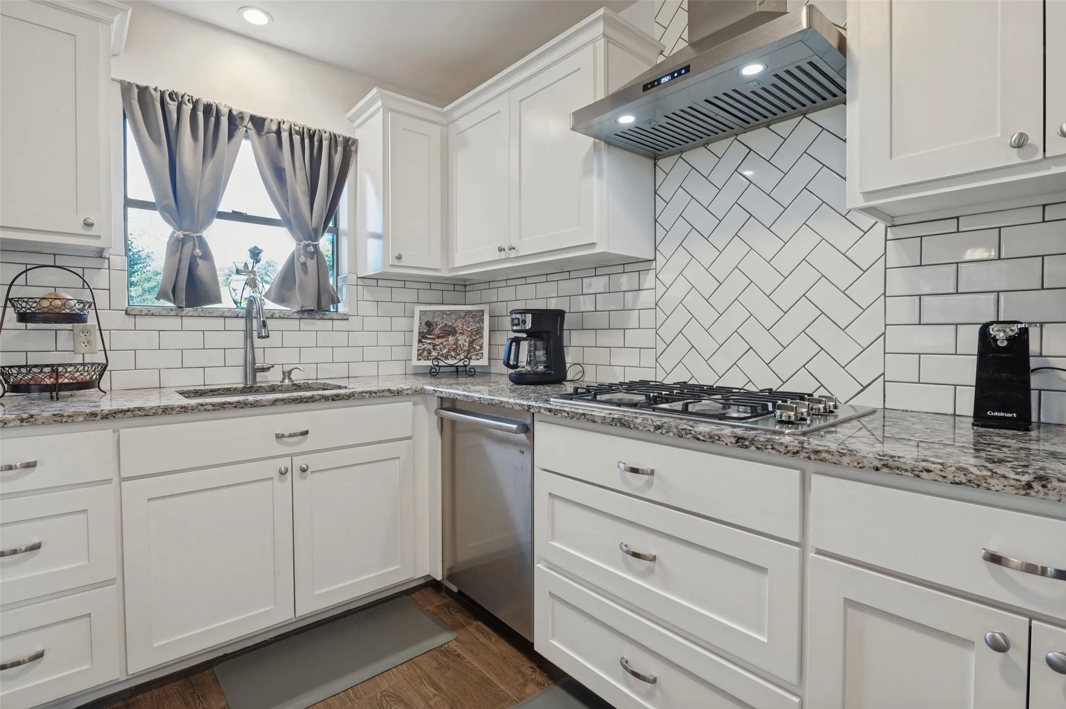 White shaker cabinetry, speckled countertops, stainless steel appliances, herringbone tile backsplash, and wood-finish flooring