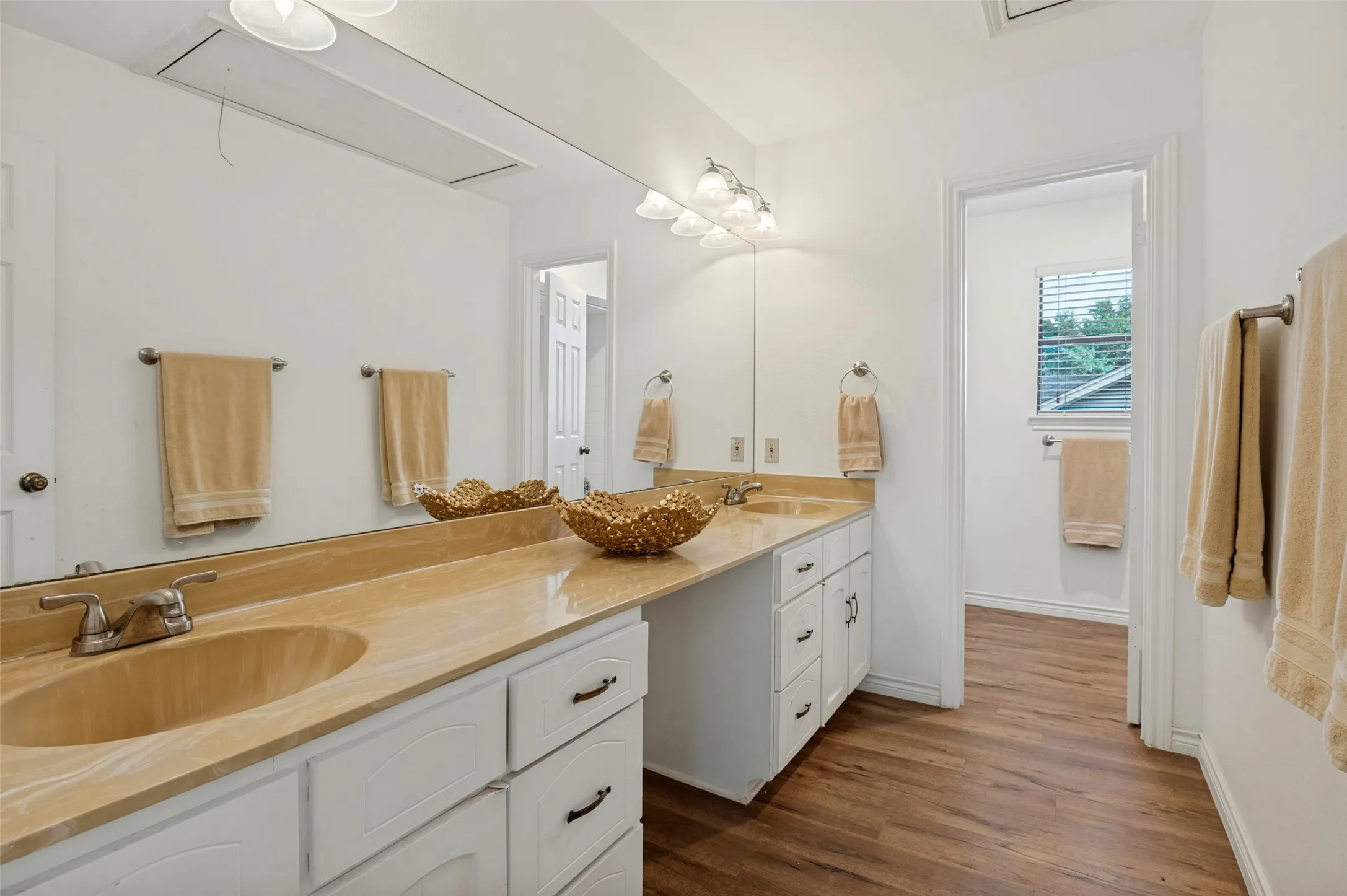 Double vanity with integrated sinks, expansive counter space, white cabinetry, and wood-finish flooring