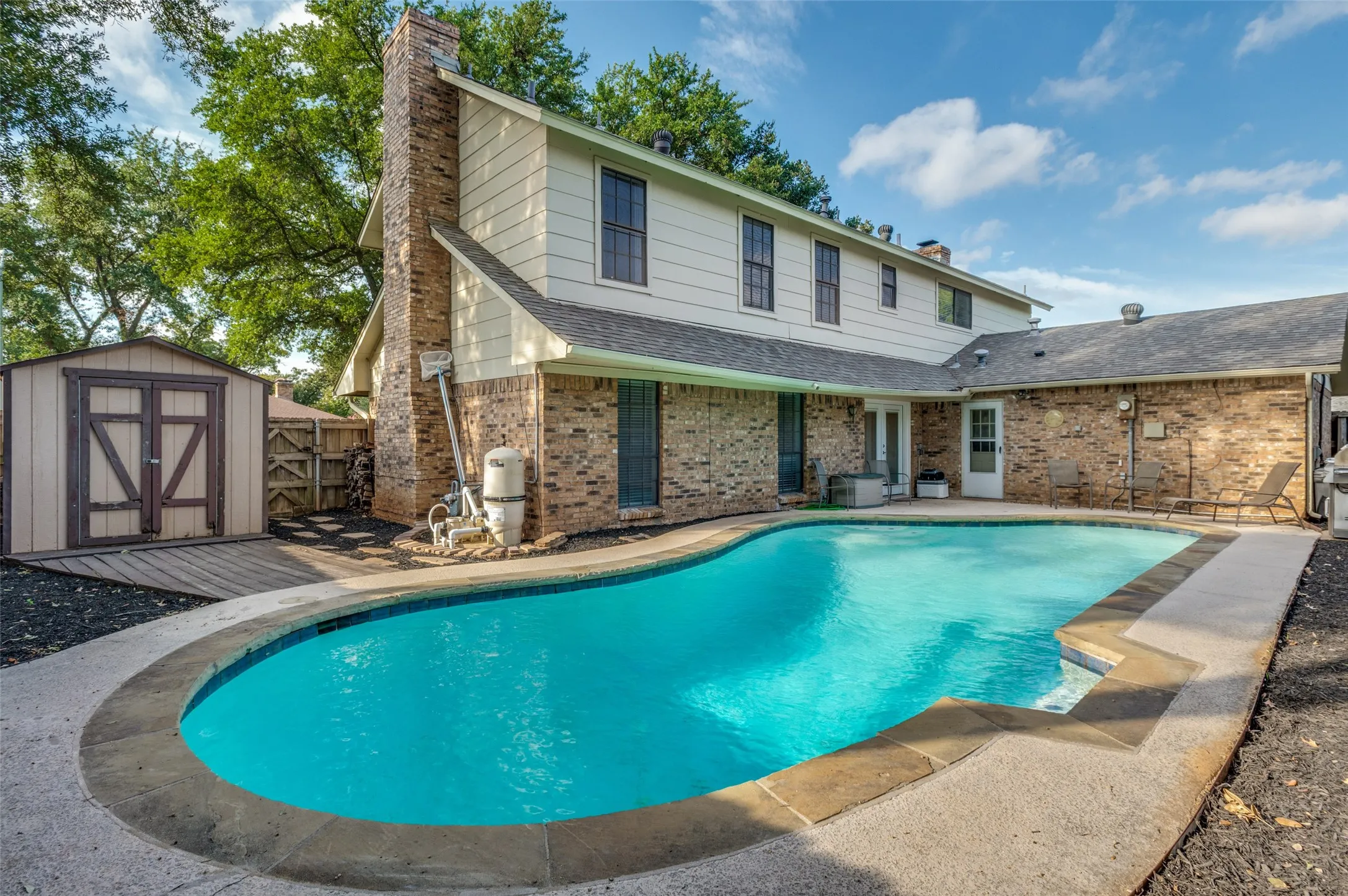 Backyard features an in-ground swimming pool with a concrete surround, brick exterior, and a detached shed