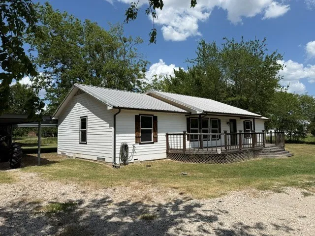 White siding exterior with a metal roof, front wood deck, and dark wood shutters