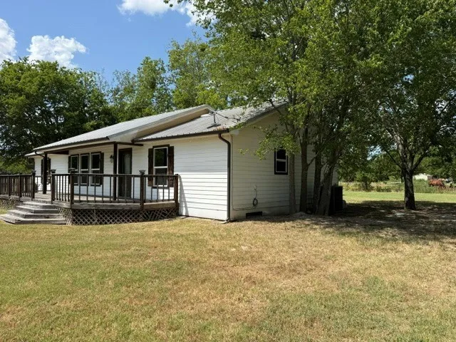 White siding exterior with a metal roof, front porch with wooden railing, and mature trees