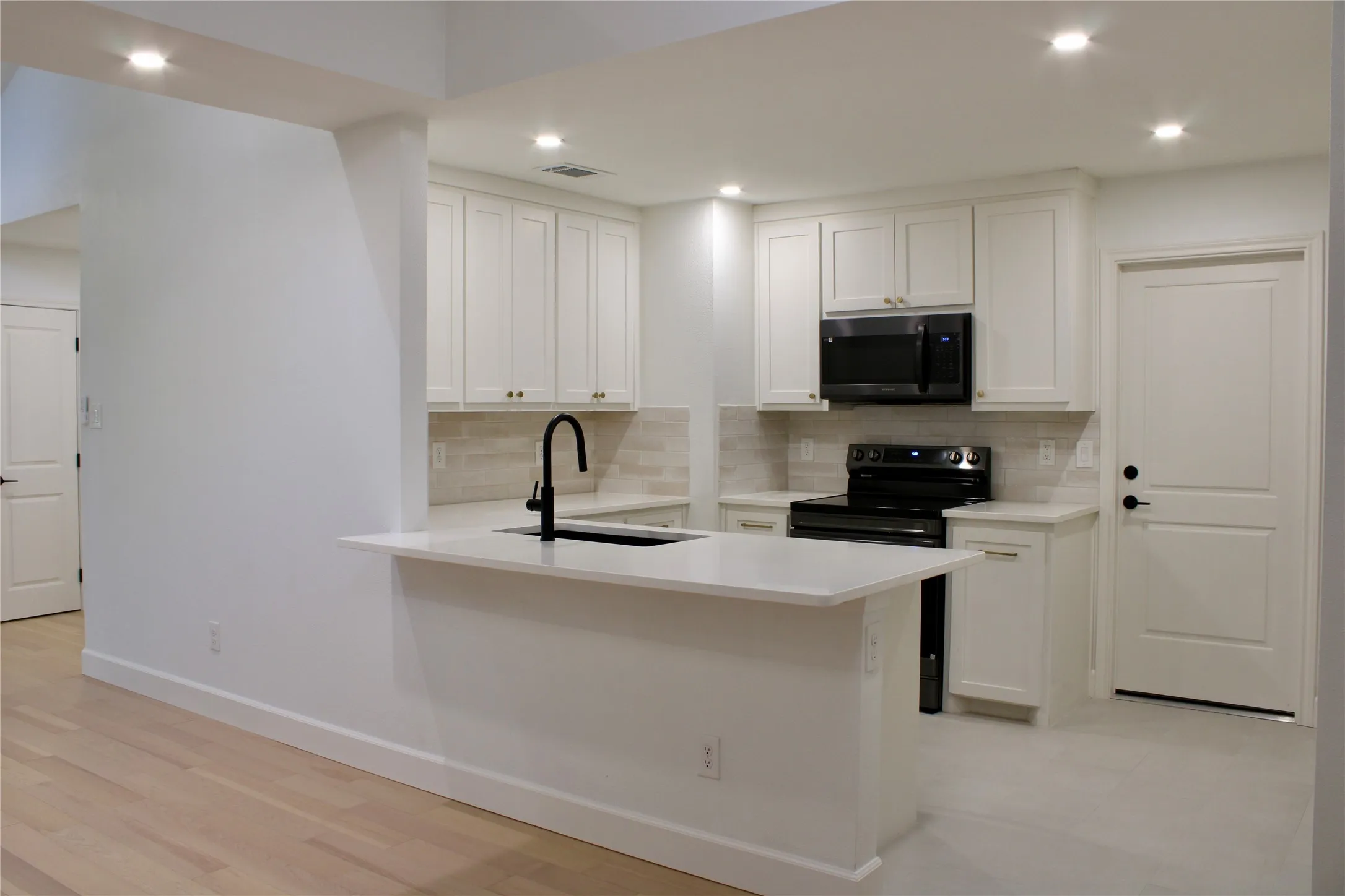 Kitchen featuring white cabinetry, light countertops, a black range, a black microwave, and recessed lighting