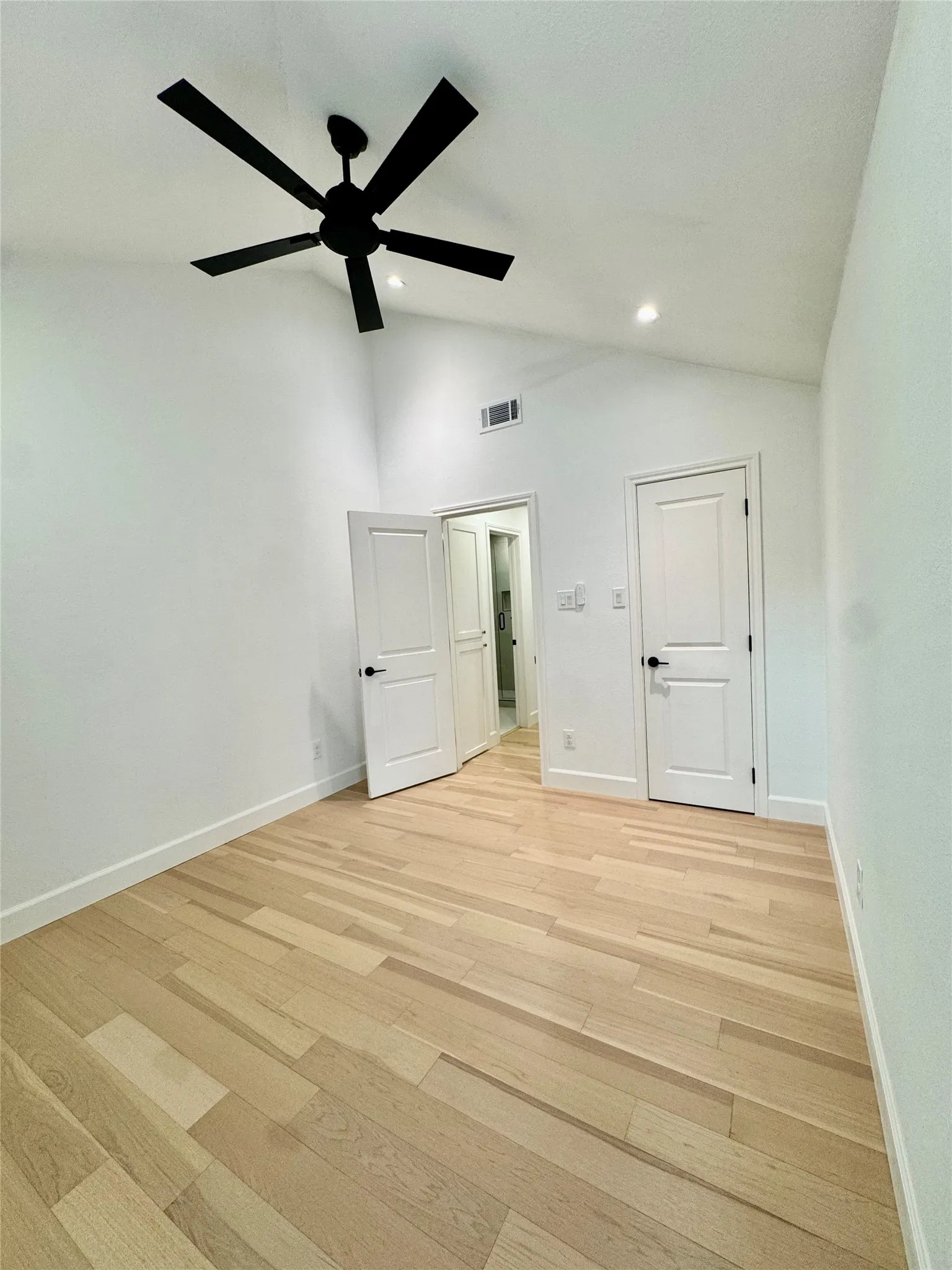 Vaulted ceiling with a black ceiling fan, recessed lighting, wood-finish flooring, and white paneled doors