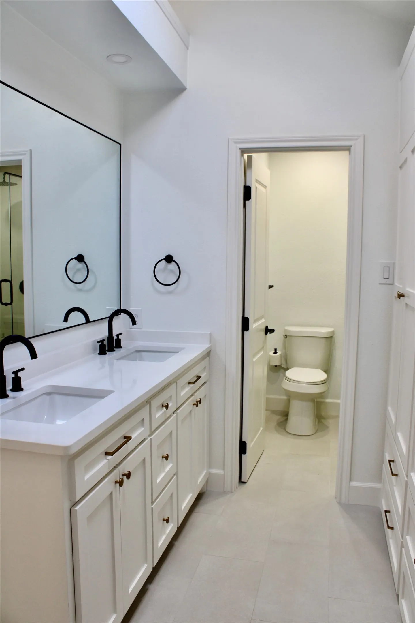 Double vanity with white cabinetry, matte black faucets, and bronze hardware