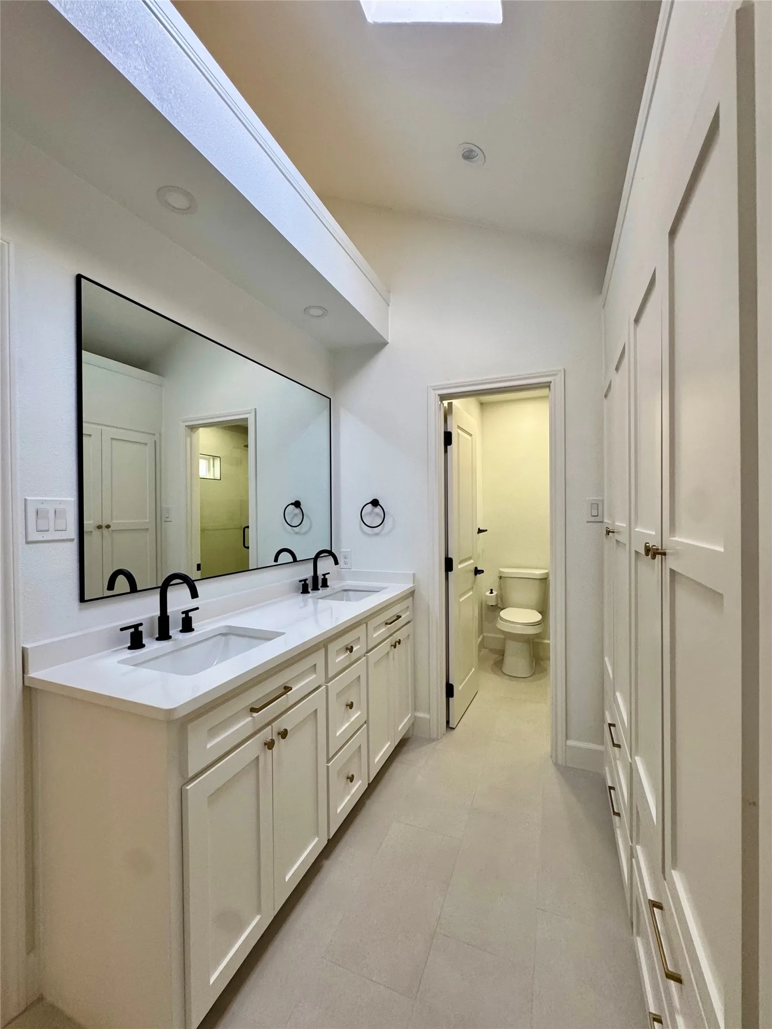Dual vanity with white shaker cabinetry, white countertop, and black fixtures
