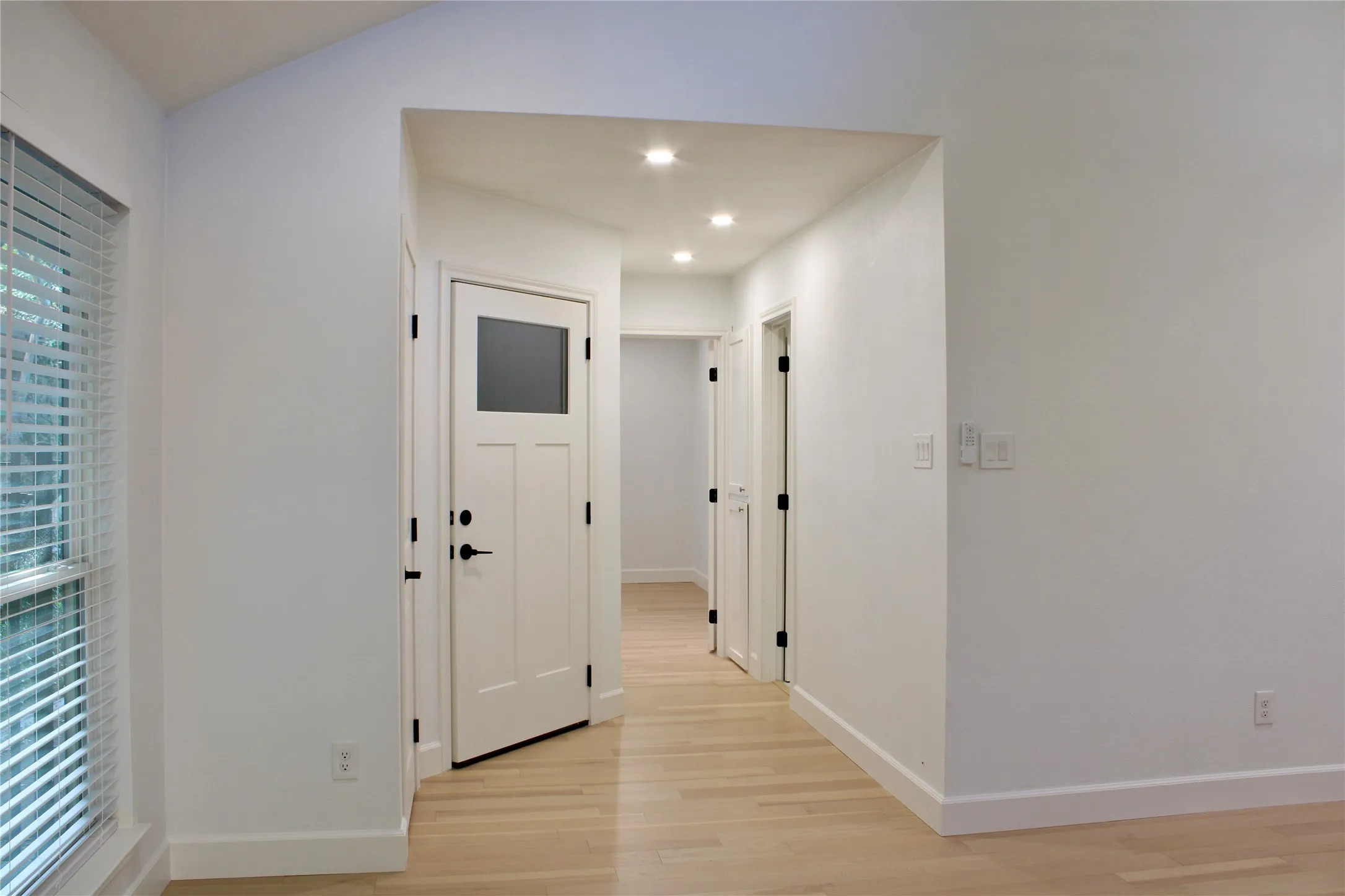 Recessed lighting illuminates the hallway, featuring light wood-finish flooring and multiple white paneled doors with matte black hardware
