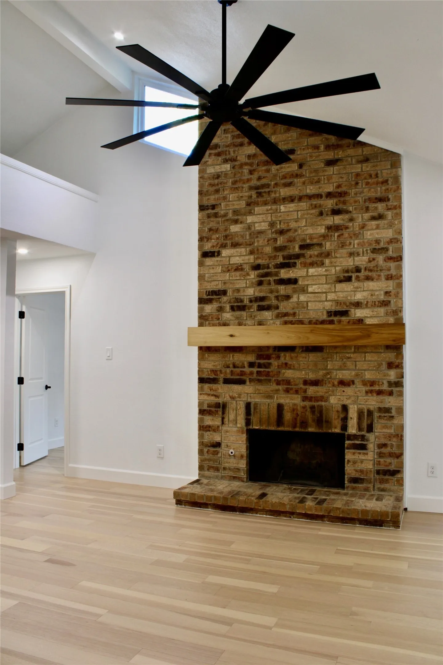 Brick-clad fireplace with a wood mantle, vaulted ceiling with an exposed beam, and a multi-blade ceiling fan