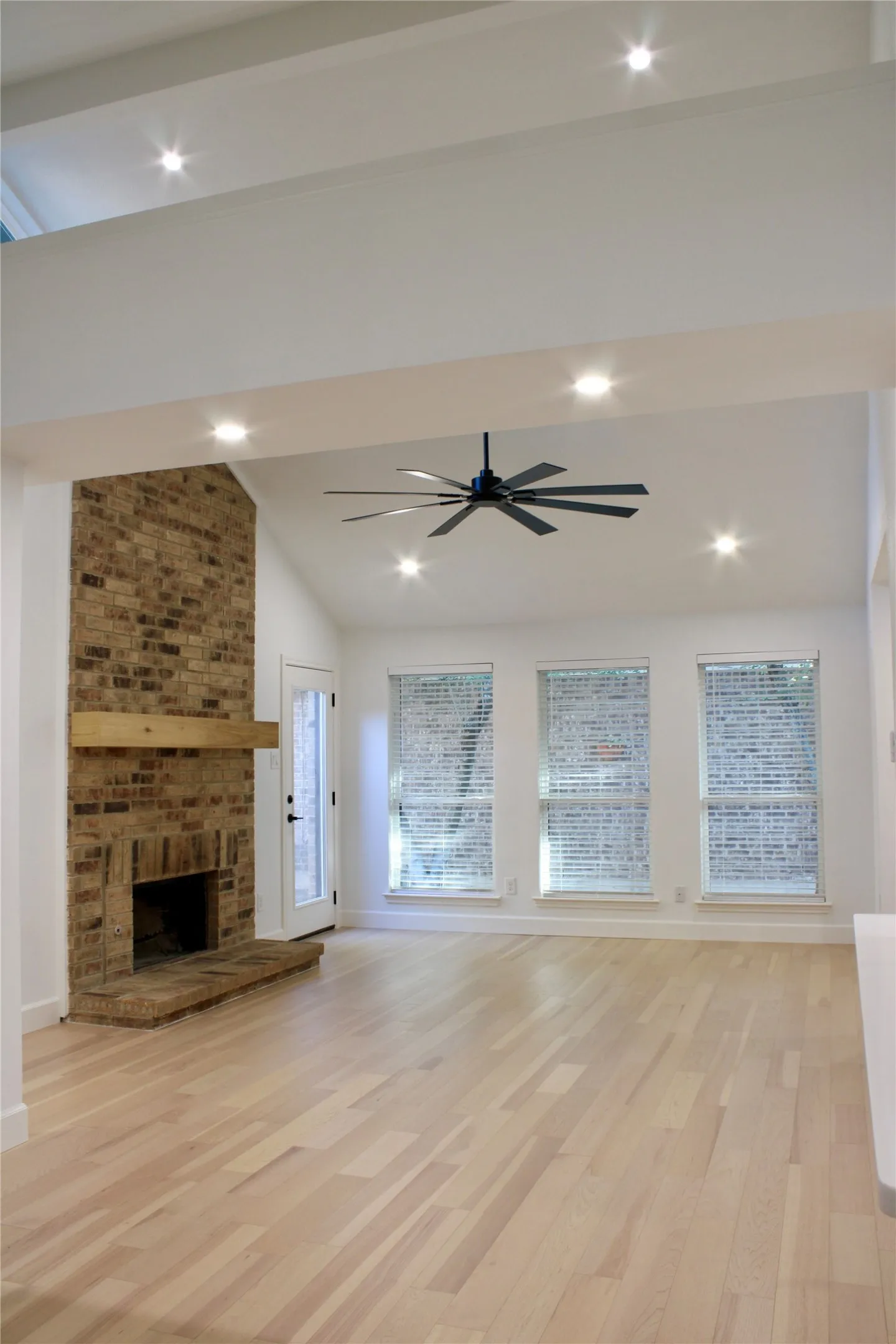 Vaulted ceiling with recessed lighting, brick fireplace with wood mantel, light wood-finish flooring, and multiple windows