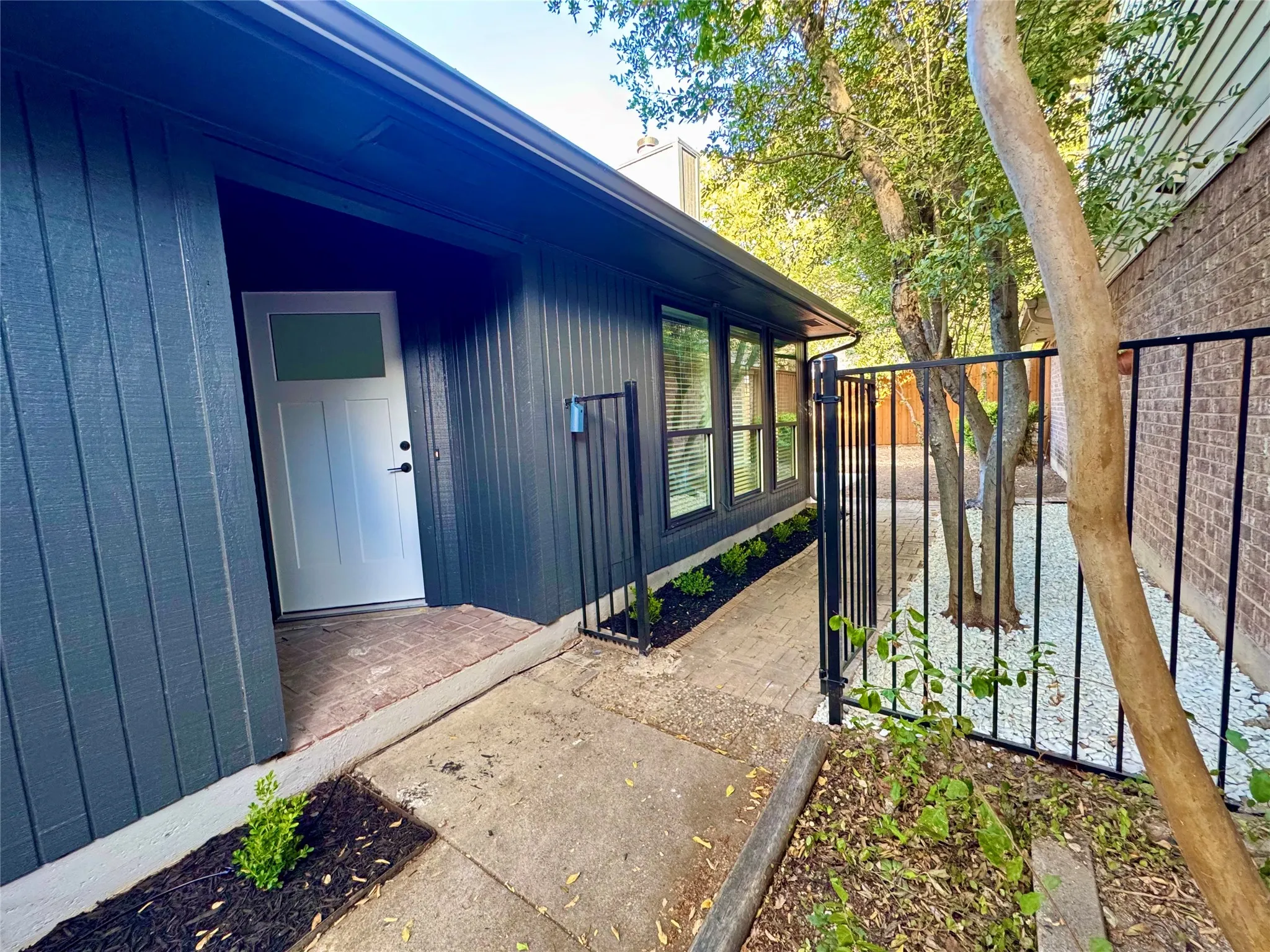 Vertical siding exterior with a white entry door, multiple windows, and a black wrought iron fence