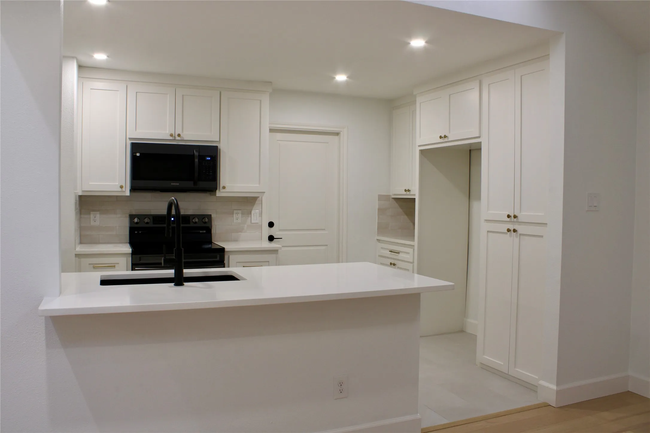 Kitchen featuring white shaker cabinetry, an integrated kitchen island with a dark basin sink, black appliances, recessed lighting, and tile flooring