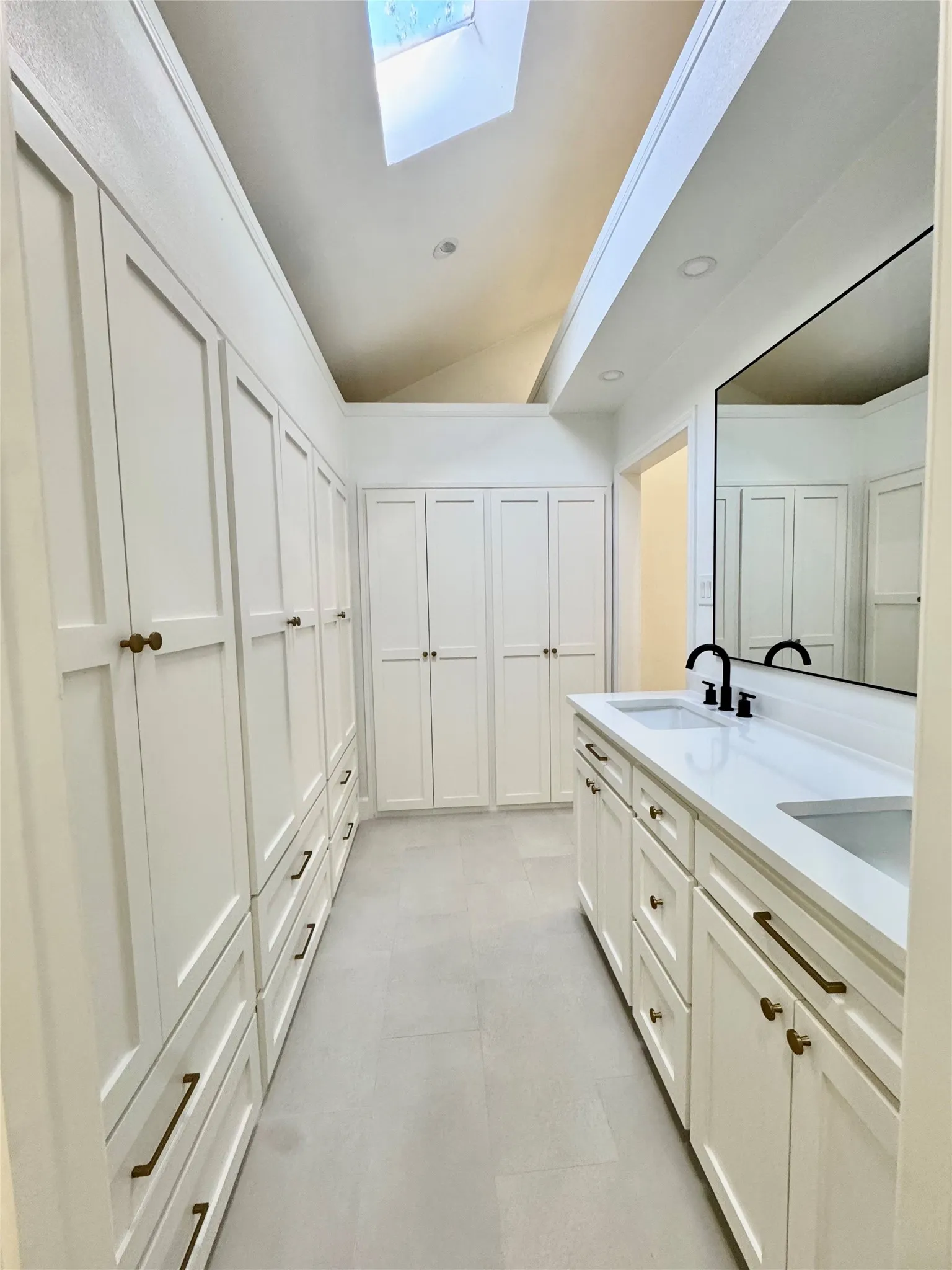 Dual skylights, extensive built-in cabinetry, dual vanity with undermount sinks, and matte black plumbing fixtures