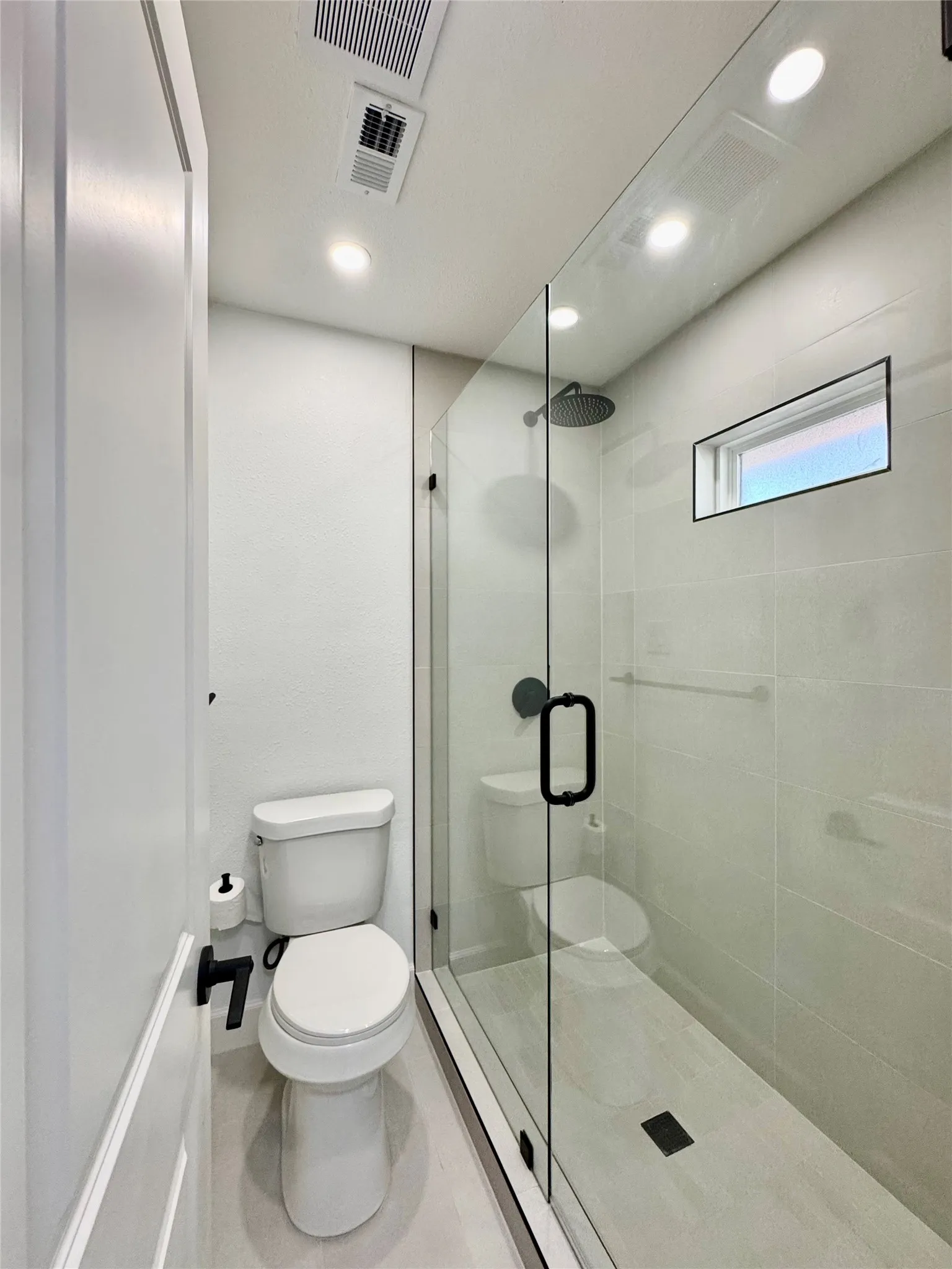 Glass-enclosed shower with a rainfall showerhead, tiled walls, and a linear drain