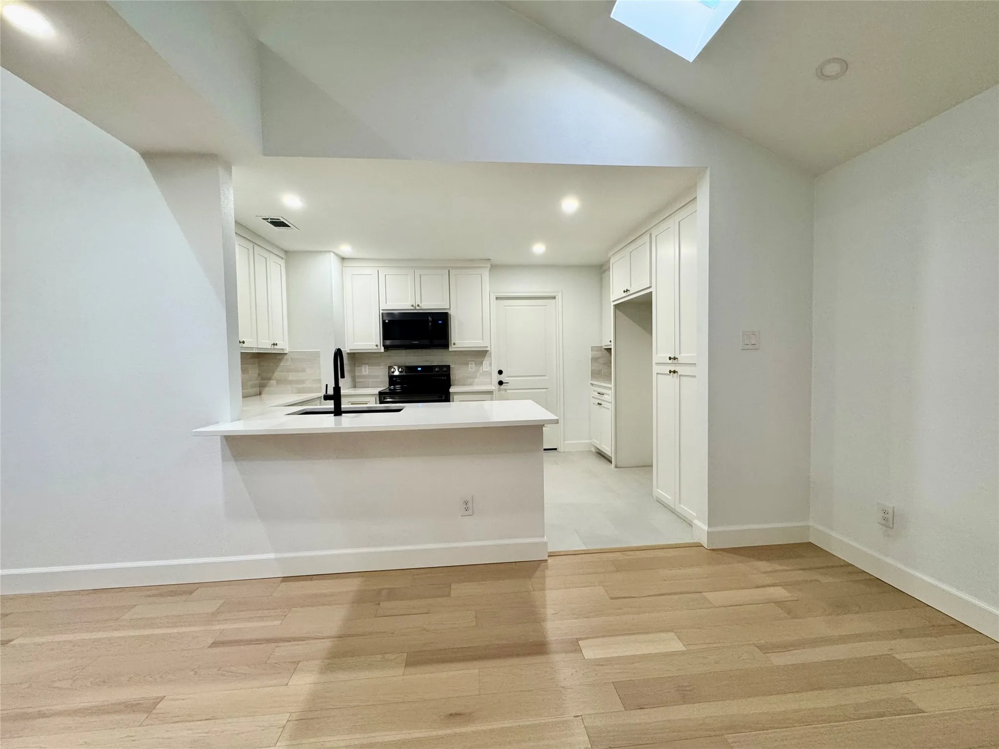 Open concept kitchen with white cabinetry, built-in appliances, a breakfast bar, and wood-finish flooring
