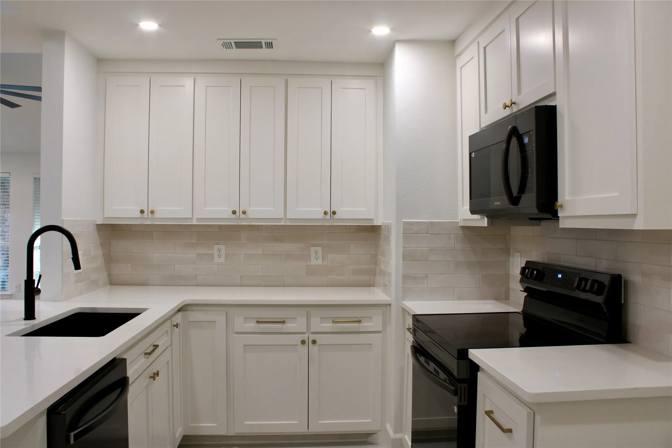 White shaker cabinetry, light-toned backsplash, black appliances, solid surface countertops, and recessed lighting