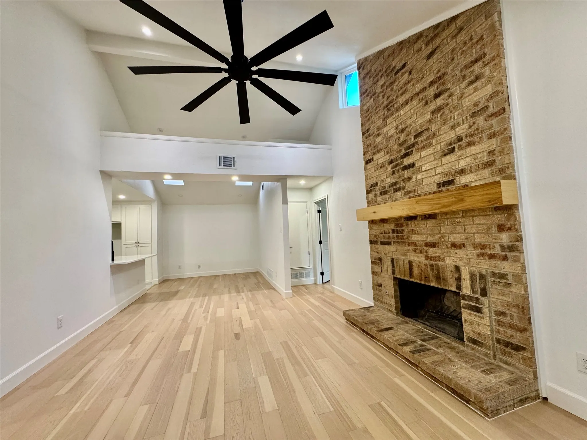 Vaulted ceiling, exposed brick fireplace with wood mantel, wood-finish flooring, large ceiling fan, and recessed lighting
