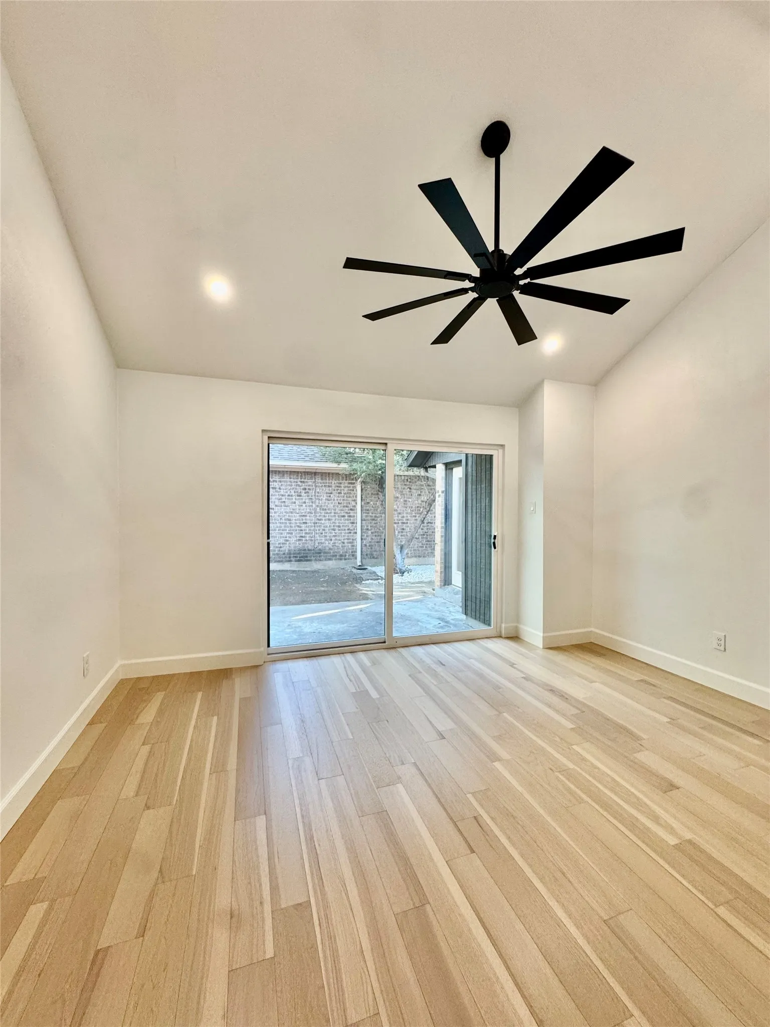 Vaulted ceiling with recessed lighting, wood-finish flooring, modern black ceiling fan, and sliding glass door
