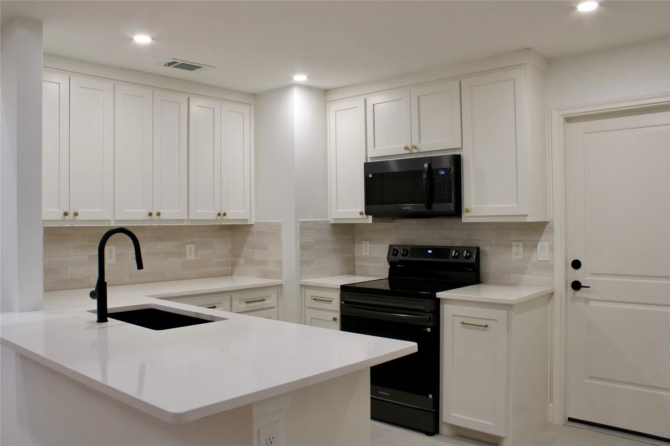 Kitchen featuring white shaker-style cabinetry, light-toned tiled backsplash, white countertops, a large black sink with a matte black faucet, and black appliances