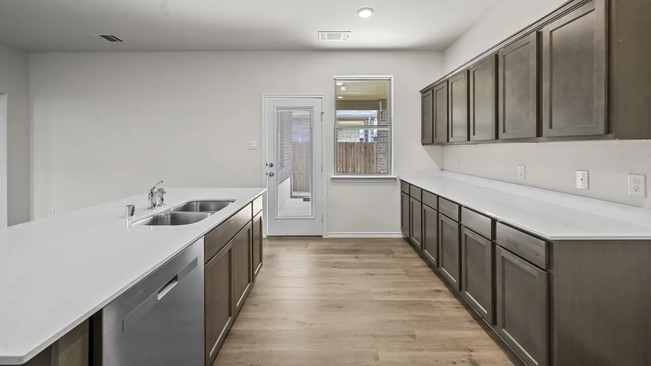 Modern kitchen with extensive dark wood-finish cabinetry, light-toned countertops, a stainless-steel dishwasher, and wood-finish flooring