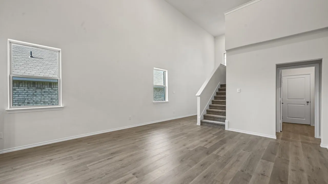 High vaulted ceilings, wood-finish flooring, two large windows, a carpeted staircase, and a paneled interior door