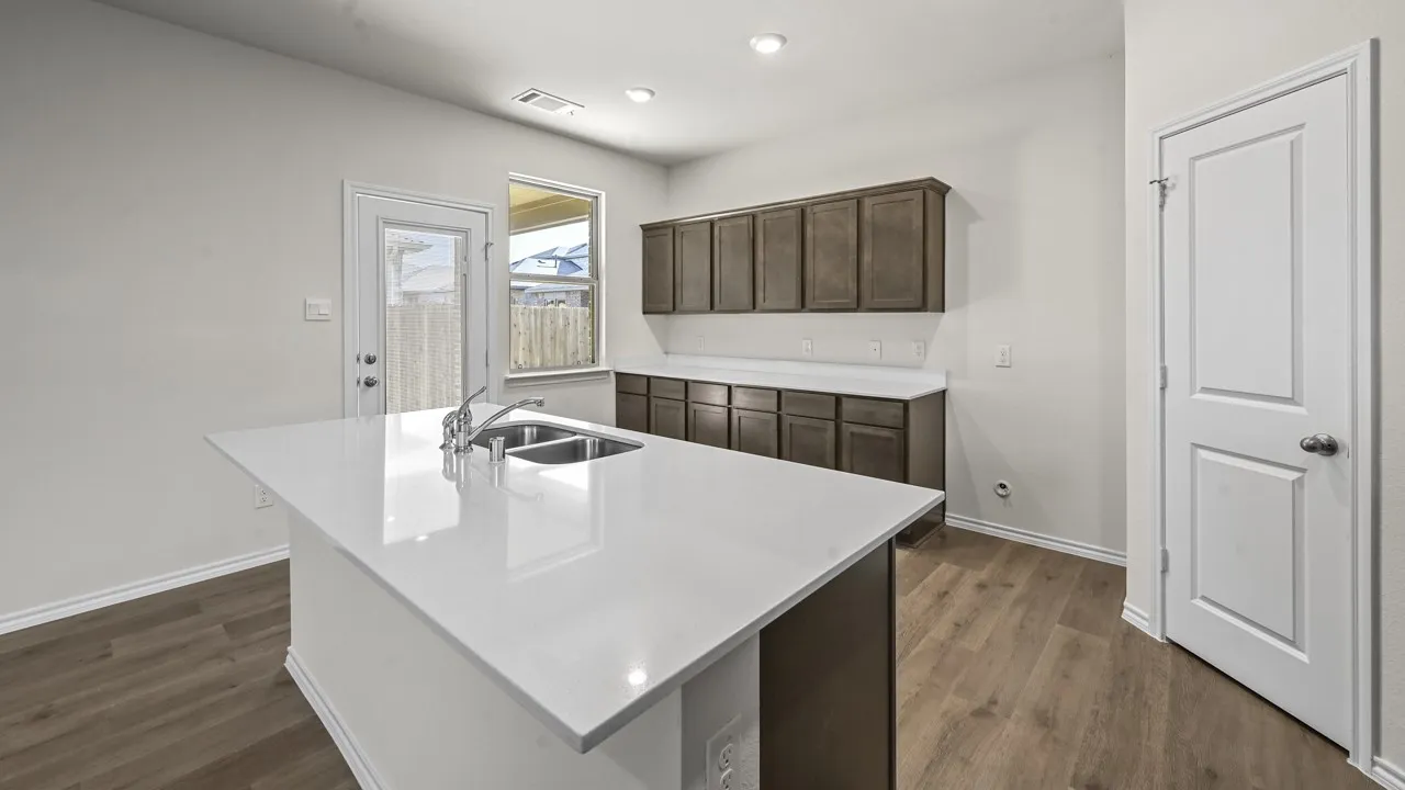 Kitchen island with a double basin sink and chrome faucet, wood-finish flooring, white countertops, and dark wood-finish cabinetry